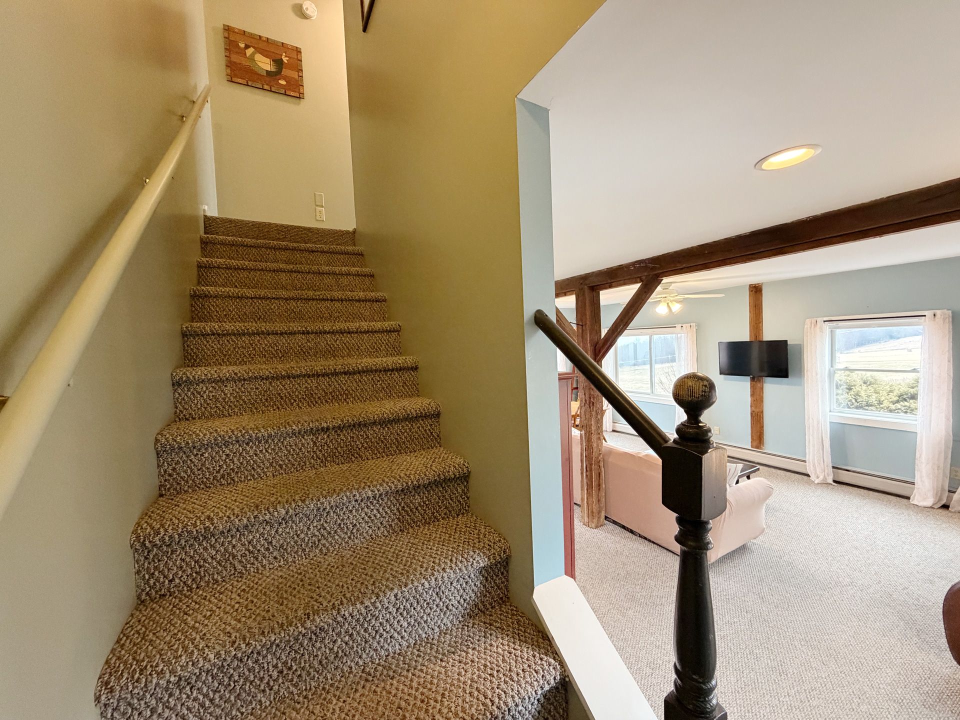 Carpeted staircase with wooden banister overlooking a bright room with a window and ceiling light.