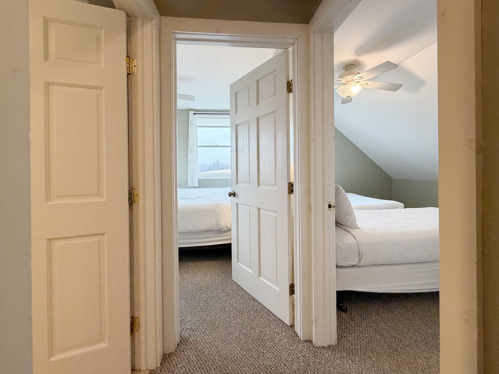 Hallway with open doors leading to two white bedrooms with carpeted floors