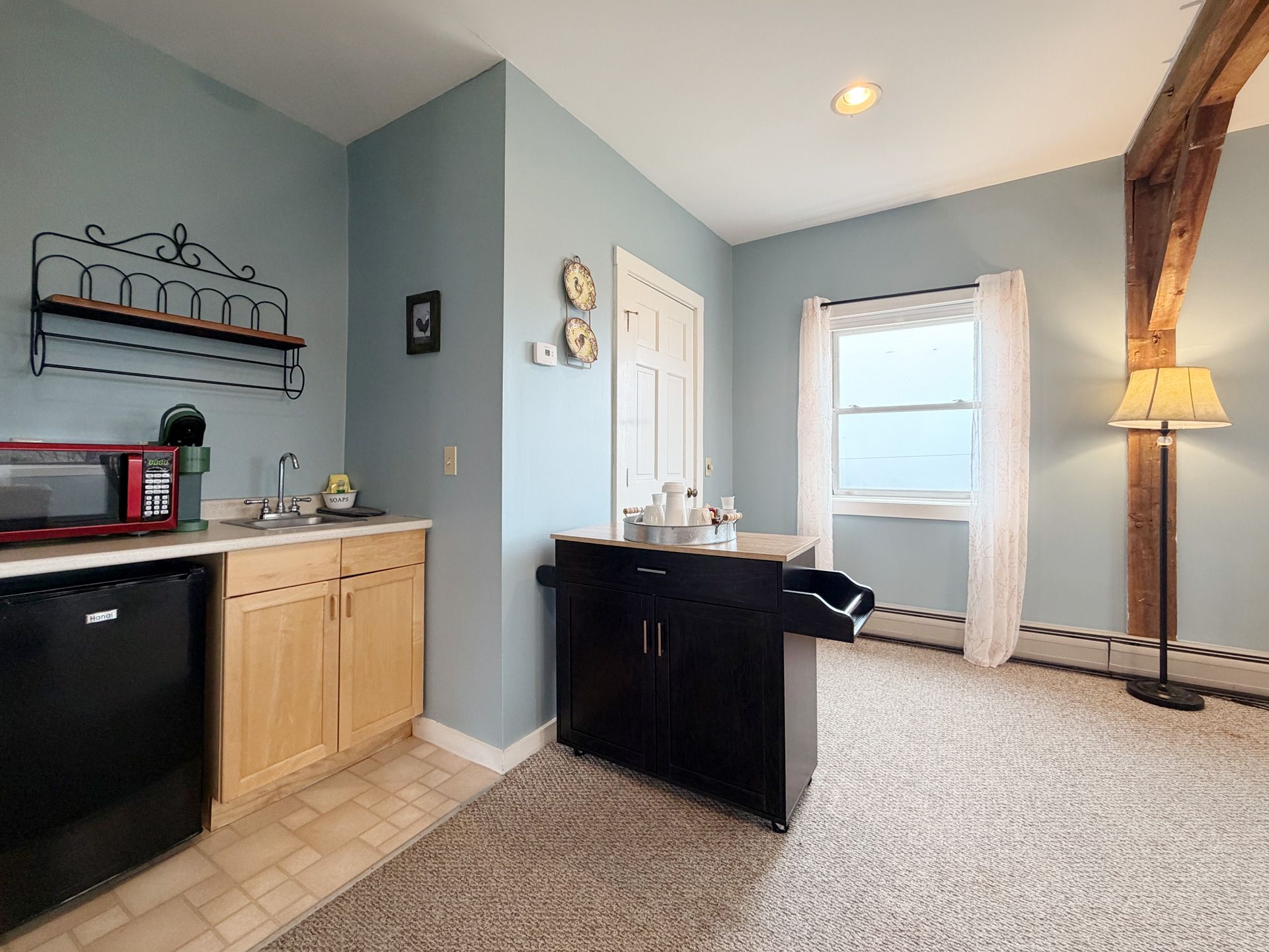 Open kitchen and living area with light blue walls, black island, carpet, and large window with sheer curtains