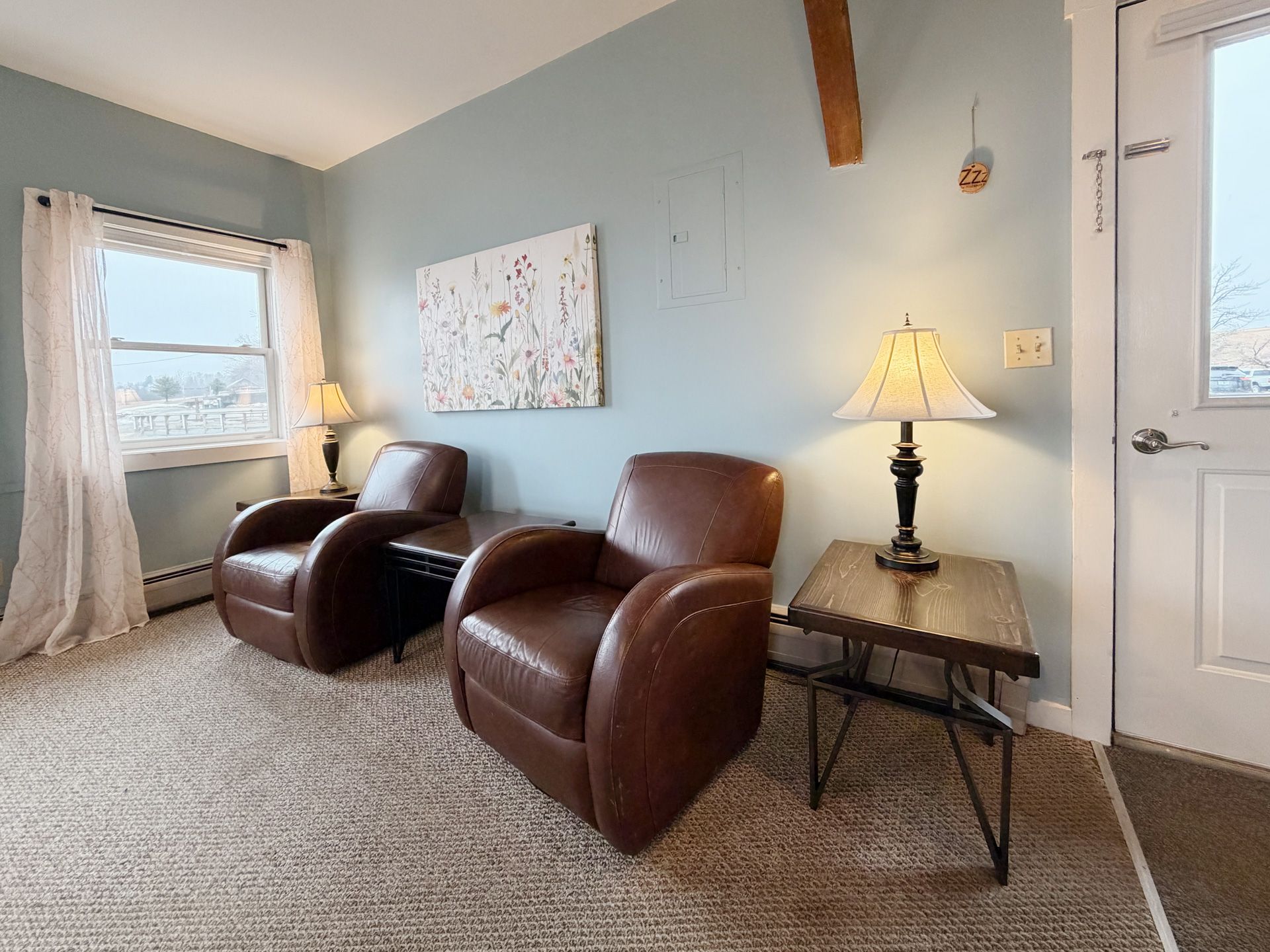 Cozy room with two brown leather chairs, a lamp on a side table, and windows with sheer curtains.
