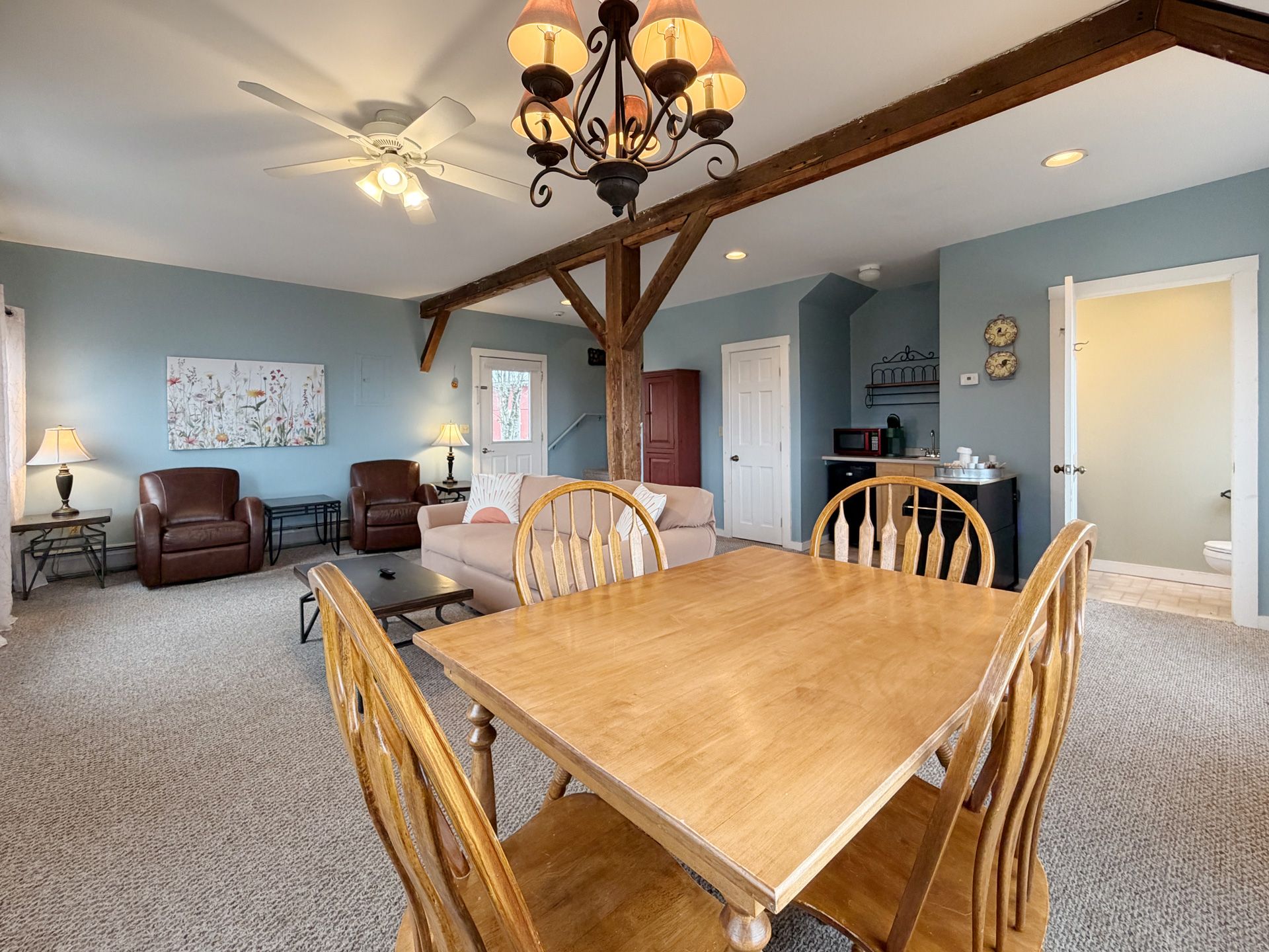 Dining area with wooden table and chairs, open to a cozy living room with leather recliners and a ceiling fan.