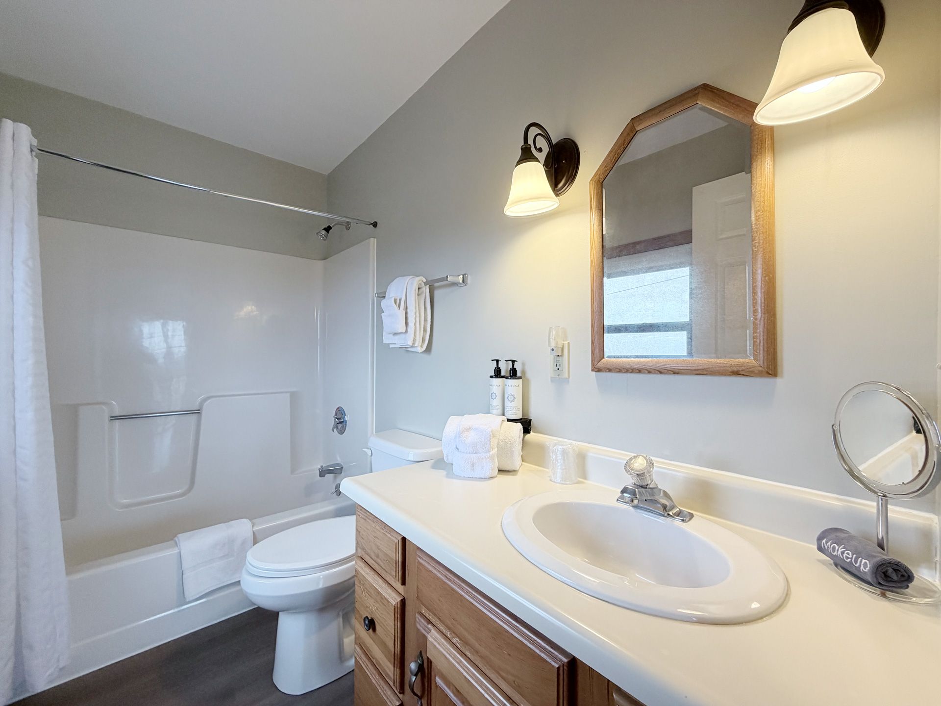 Bright bathroom with white tub, toilet, and vanity sink under wall sconces