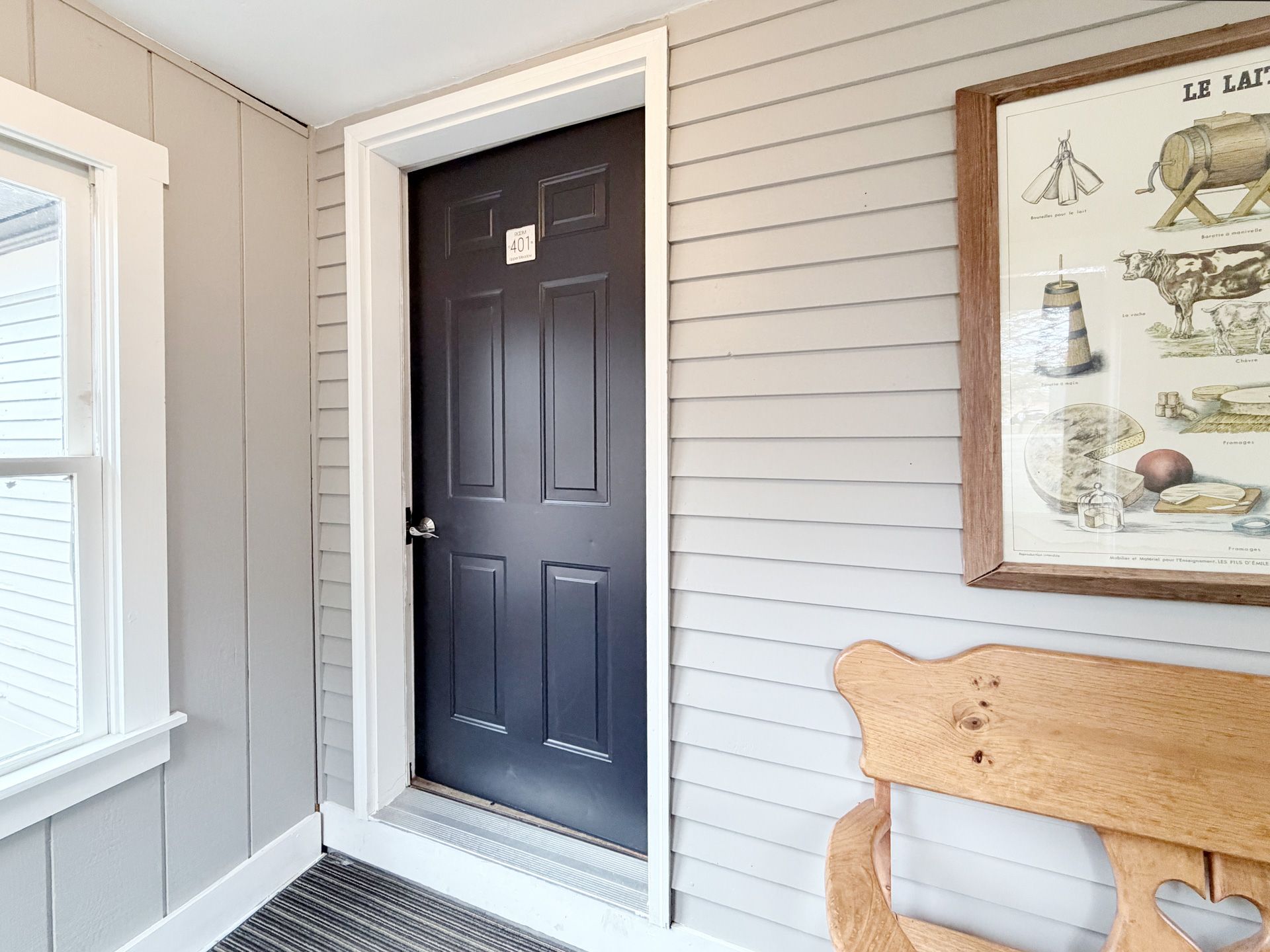 Front porch with a black front door, gray siding, and a wooden bench beside a framed wall print.