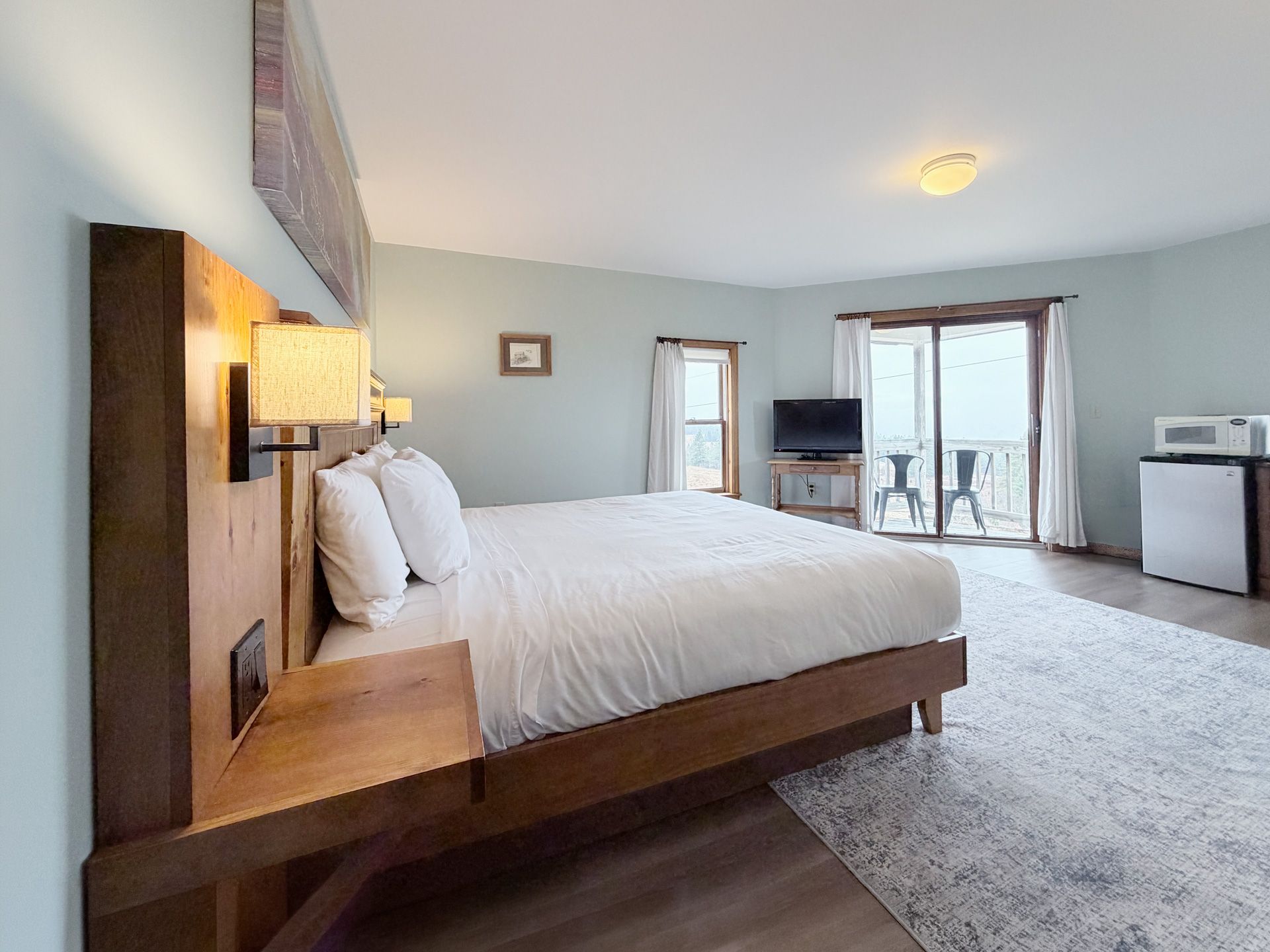 Spacious modern bedroom with a wooden bed, white bedding, and sliding doors to a balcony.