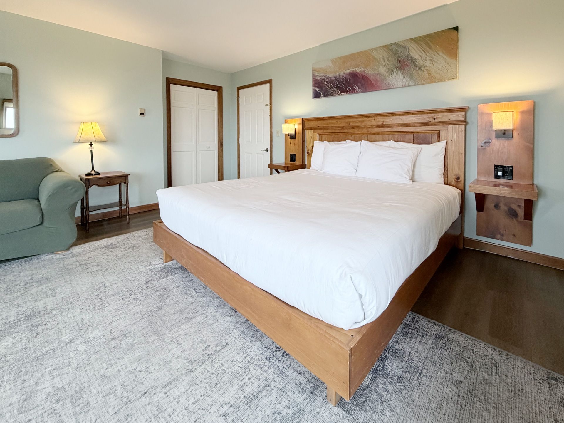 Modern bedroom with a large white bed, green sofa, bedside lamps, and soft carpet