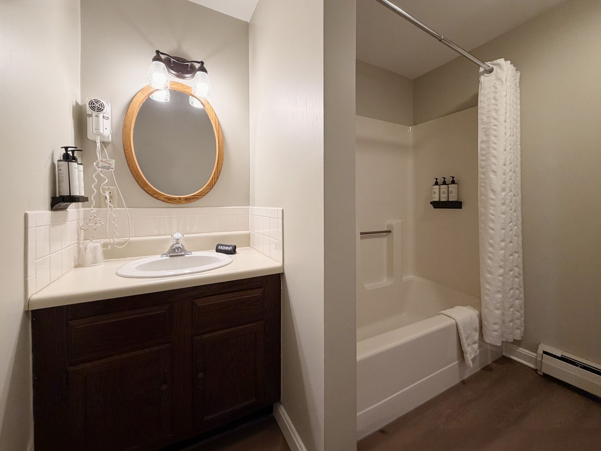 Bathroom with dark vanity, round mirror, sink, and tub with shower curtain.