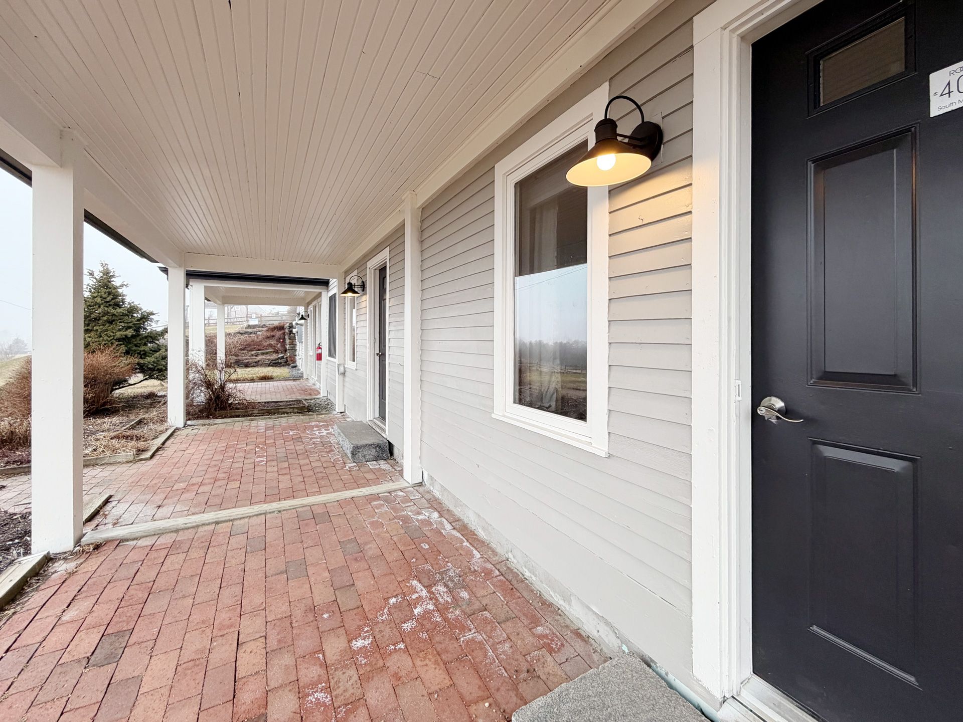 Covered brick apartment walkway with white siding, black doors, and porch lights