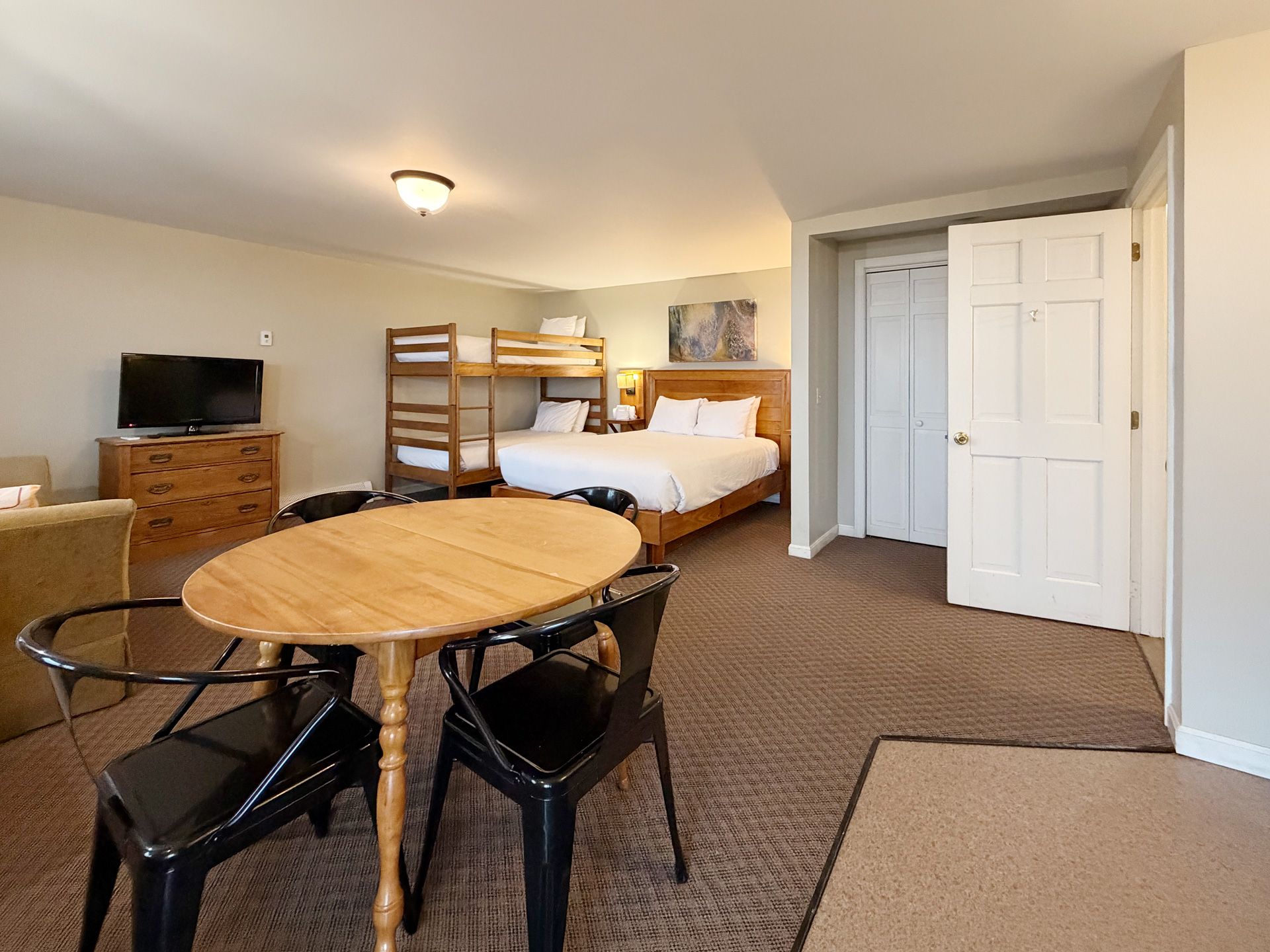 Bedroom studio with round table, black chairs, bunk bed, dresser, and open closet door.