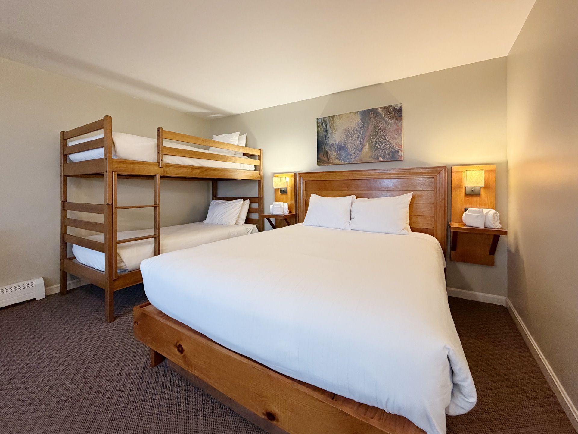 Bedroom with white bed, wooden bunk bed, and bedside lamps on warm beige walls