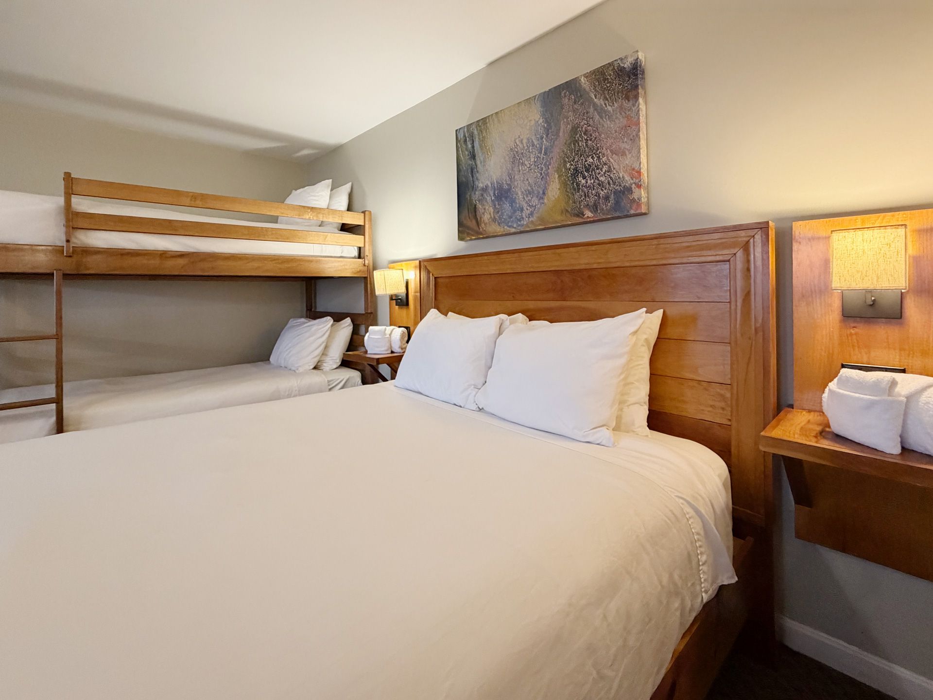 Hotel room with a king bed, bunk bed, bedside lamps, and wooden furniture