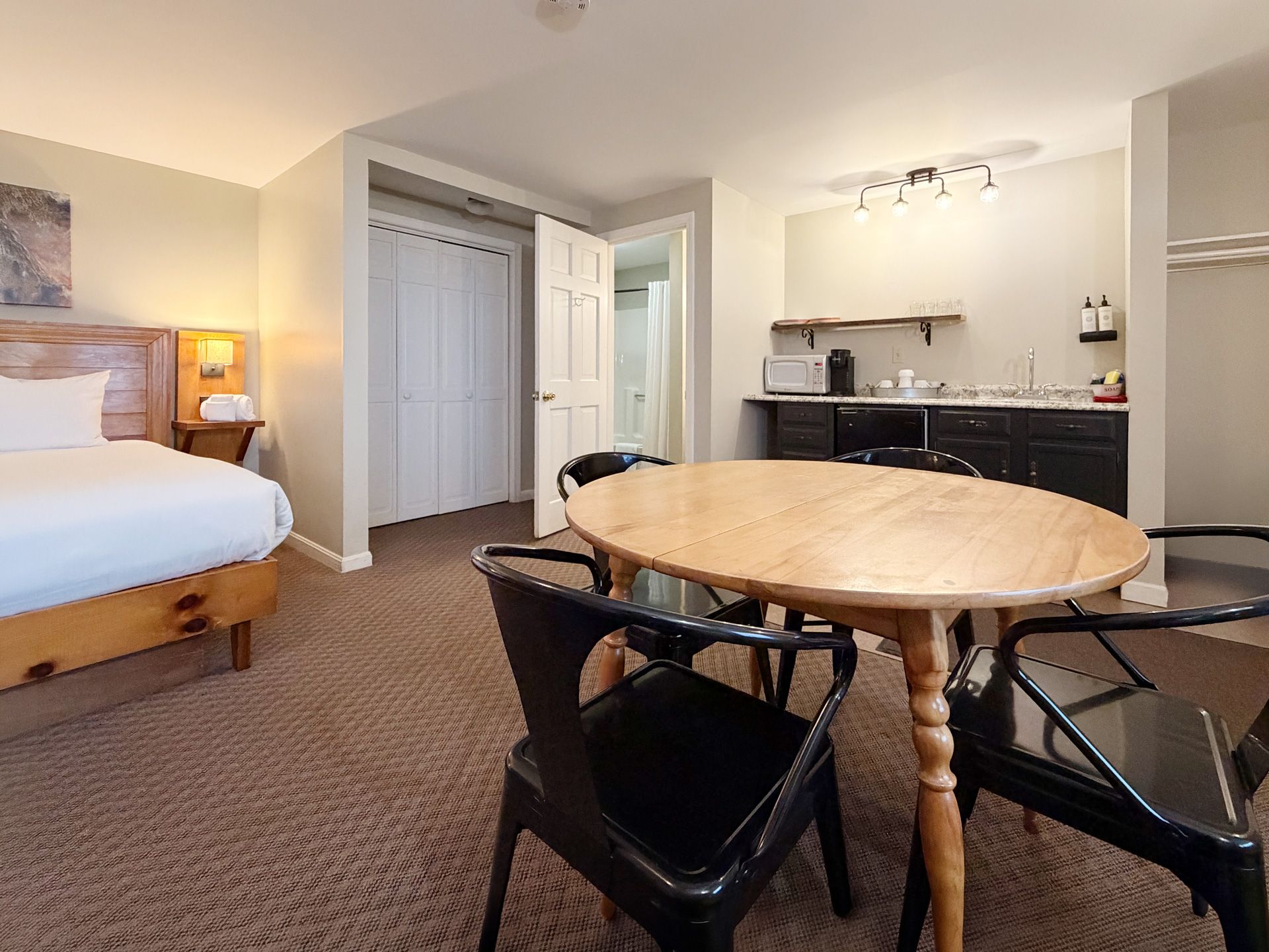 Hotel room with bed, round wooden table, chairs, and kitchenette area