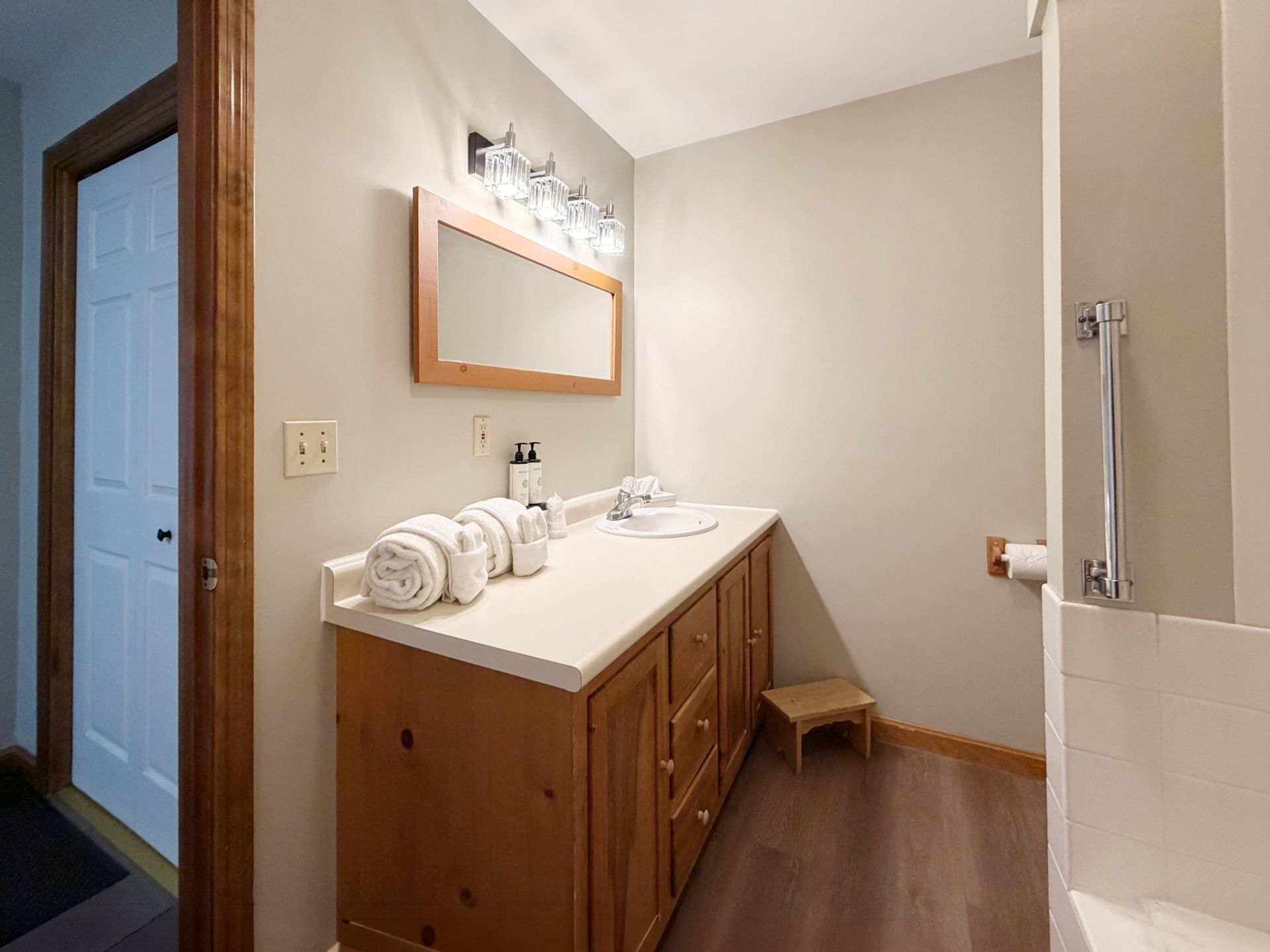 Small bathroom vanity with wood cabinet, white countertop, mirror, and towel rack in a beige room
