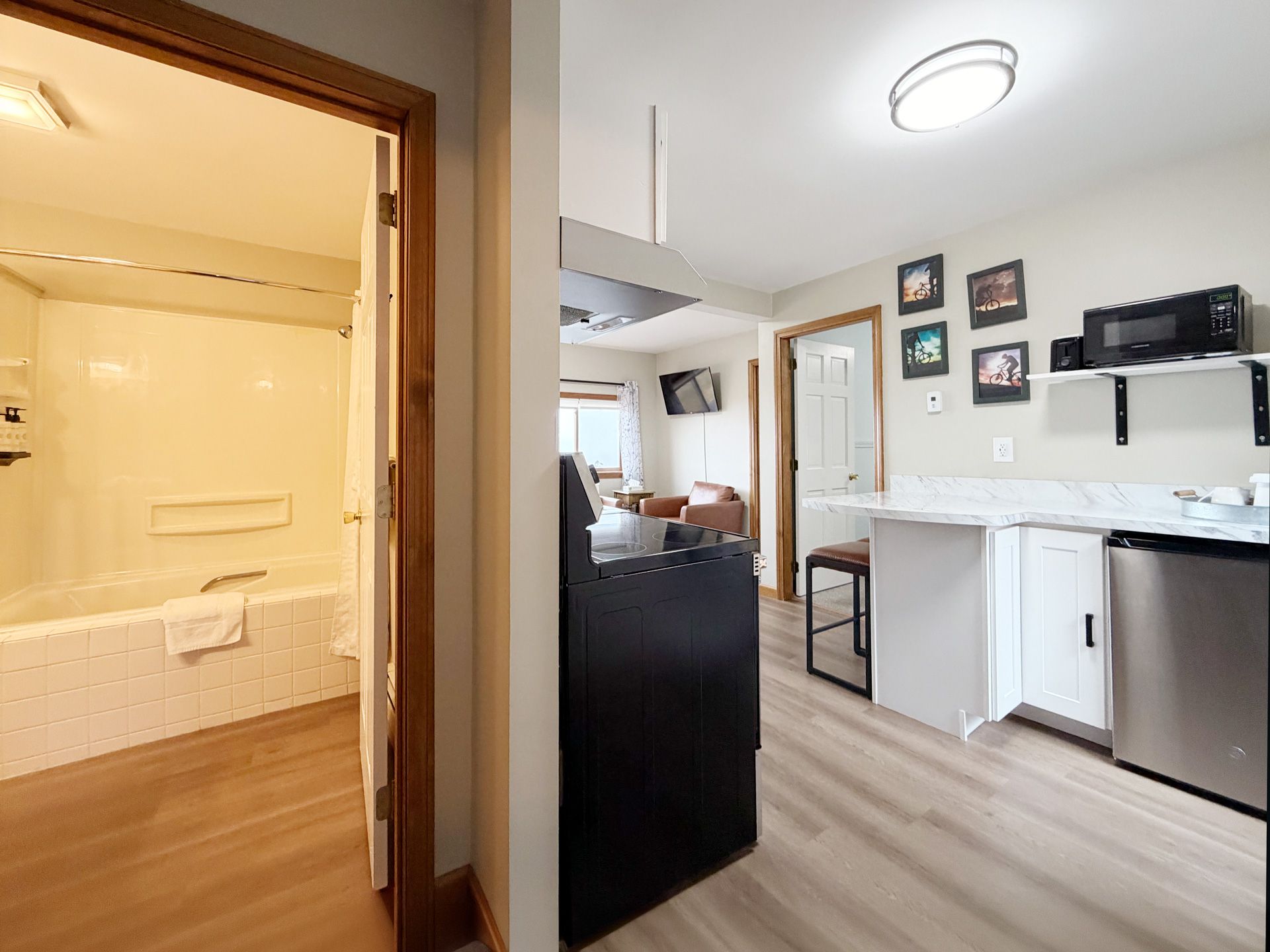 Bright kitchen and open bathroom doorway with white cabinets, wood floor, and black island cabinet.