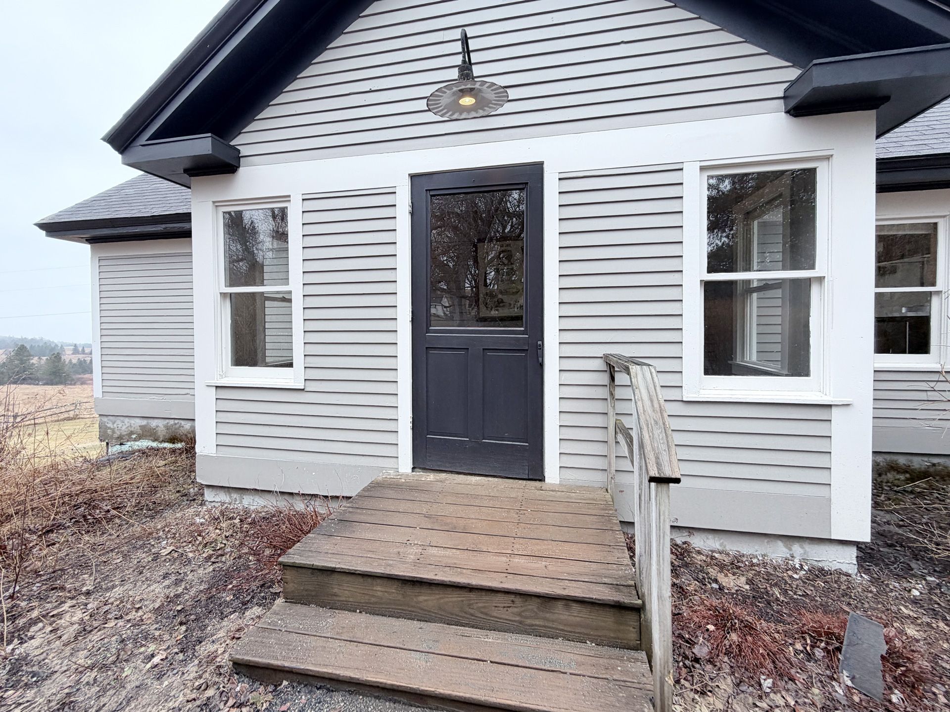 Small white house exterior with front steps, dark door, and two windows under a porch light