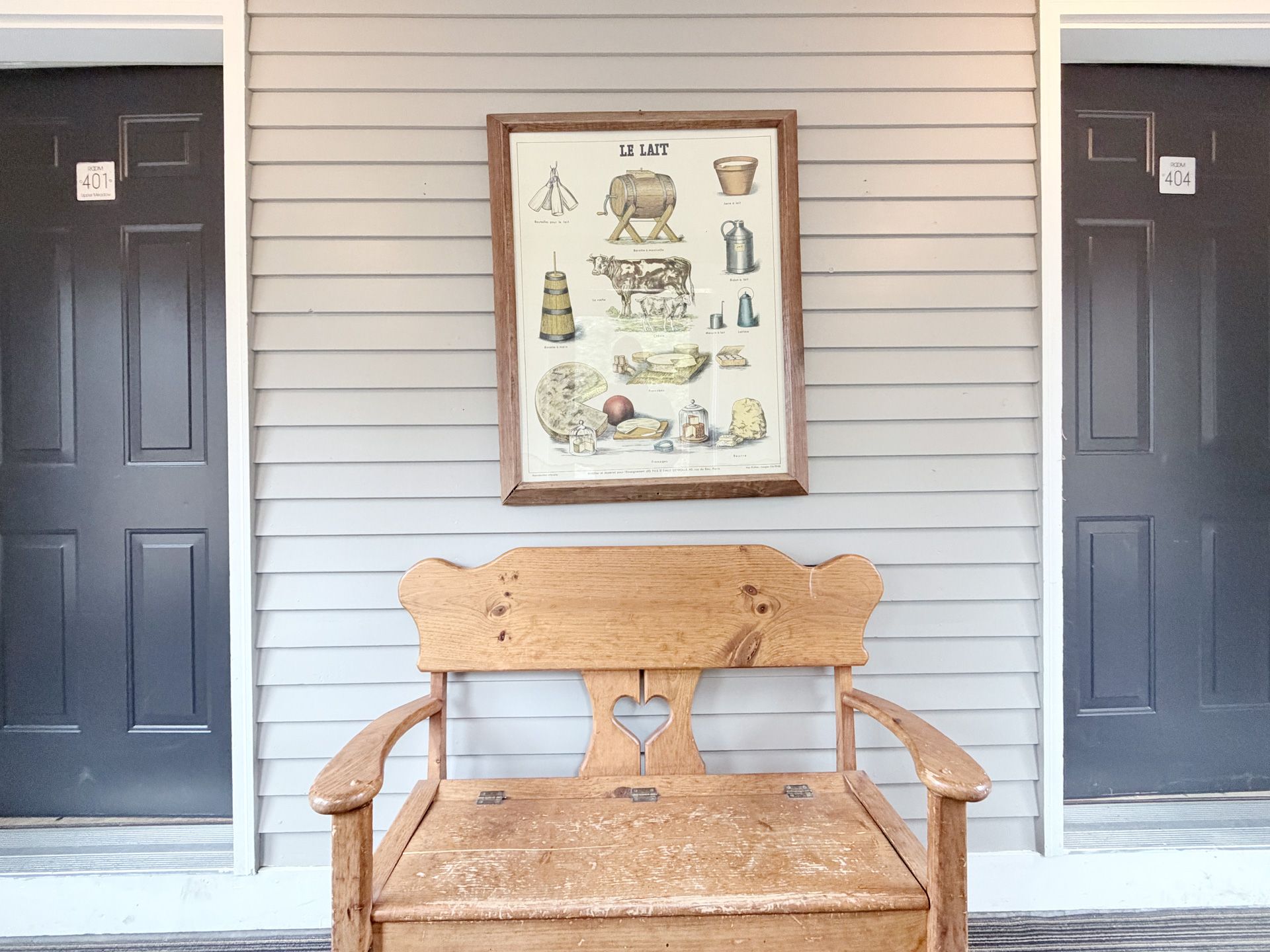 Two black doors flanking a rustic bench beneath a framed wall art display on a light siding wall.