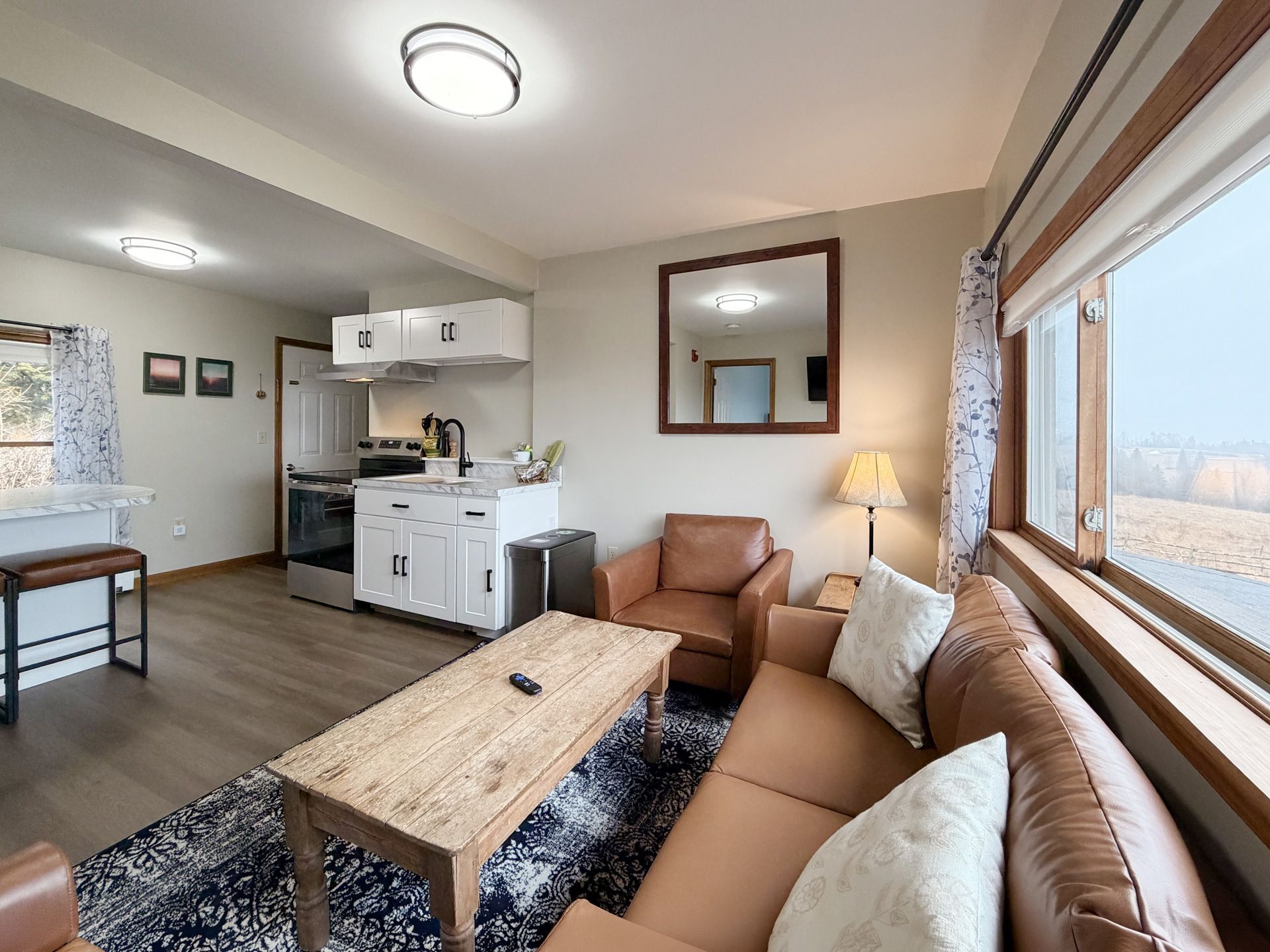 Bright living room with tan sectional, coffee table, kitchen area, and large window view