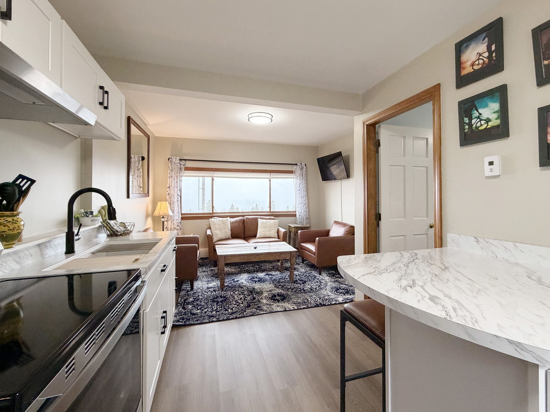 Compact kitchen opening into a cozy living room with sofa, table, window, and patterned rug.