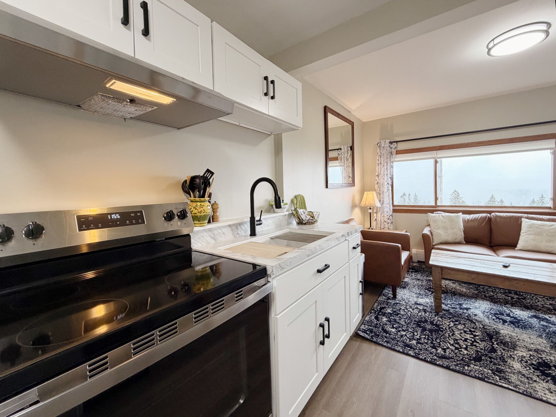 Modern kitchen opening to a cozy living room with white cabinets, black stove, and large window.