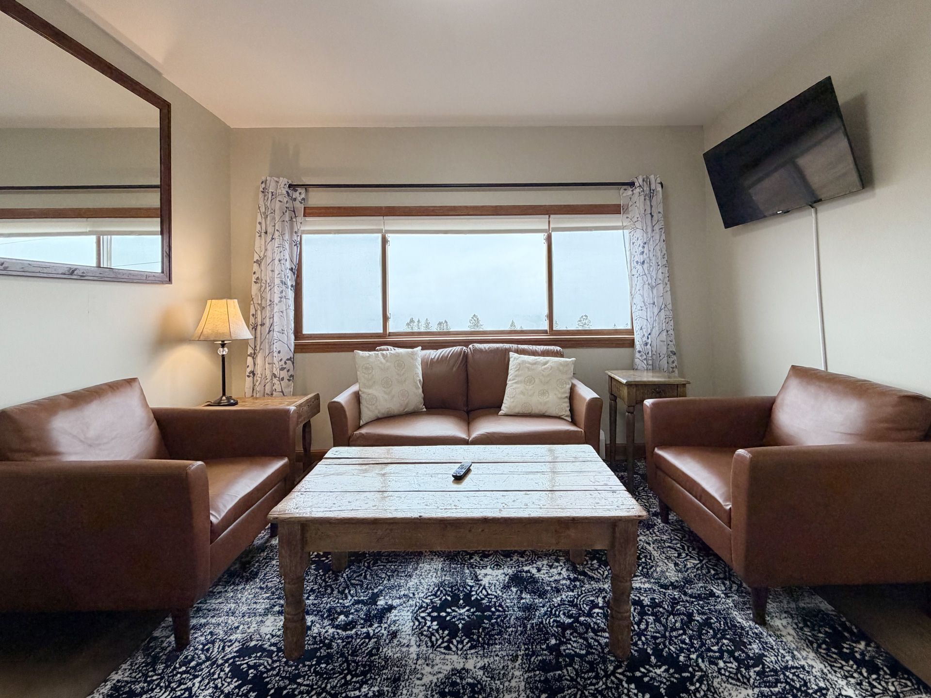 Cozy living room with brown leather sofas, patterned rug, marble coffee table, and wall-mounted TV