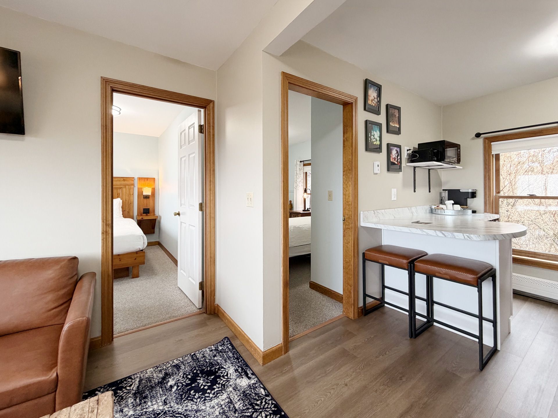 Bright living room with sofa, small desk, bar stools, and open doorways to bedroom and hallway