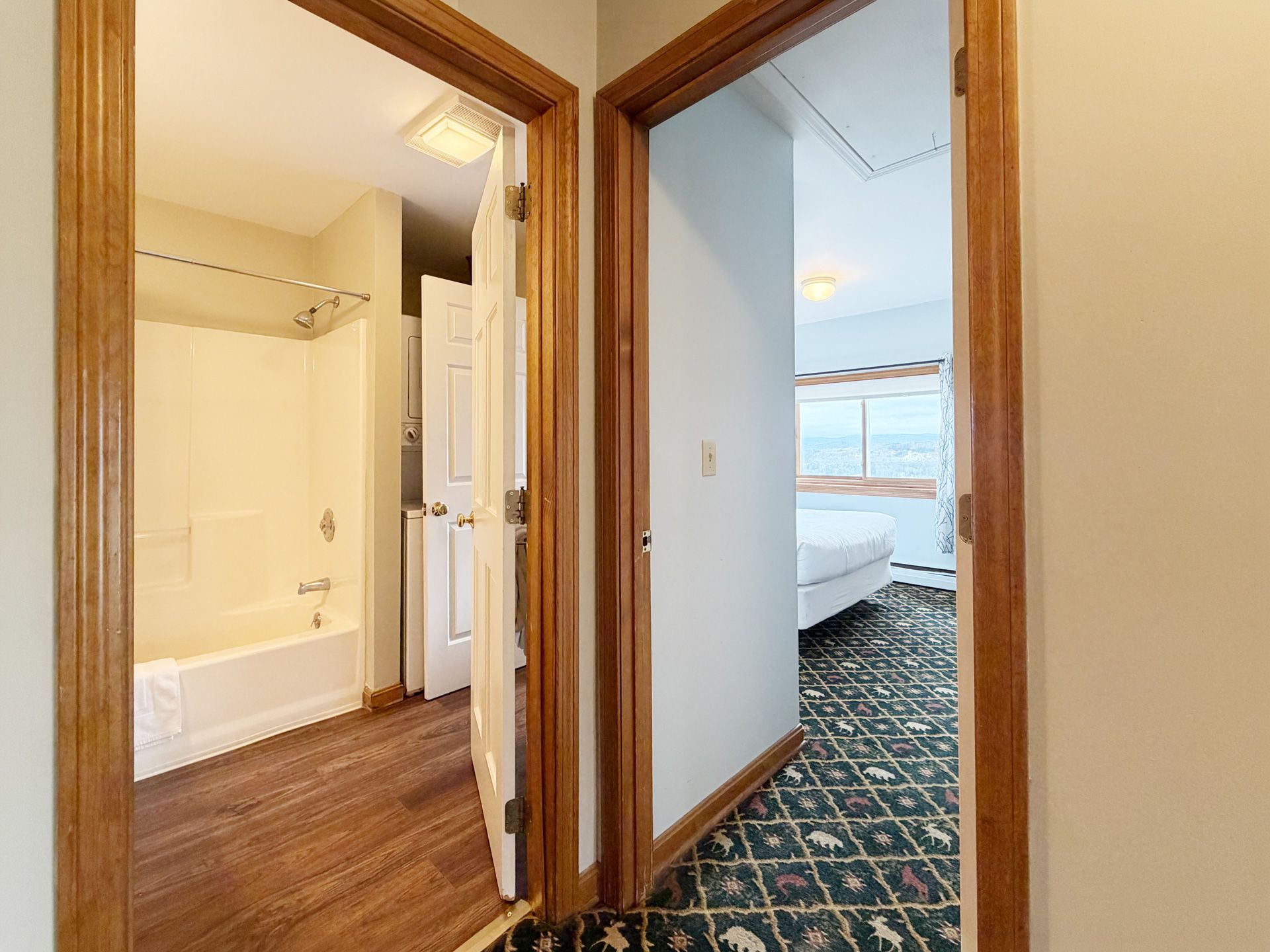 Apartment hallway with bathroom on left and bedroom on right, featuring wood trim and patterned carpet