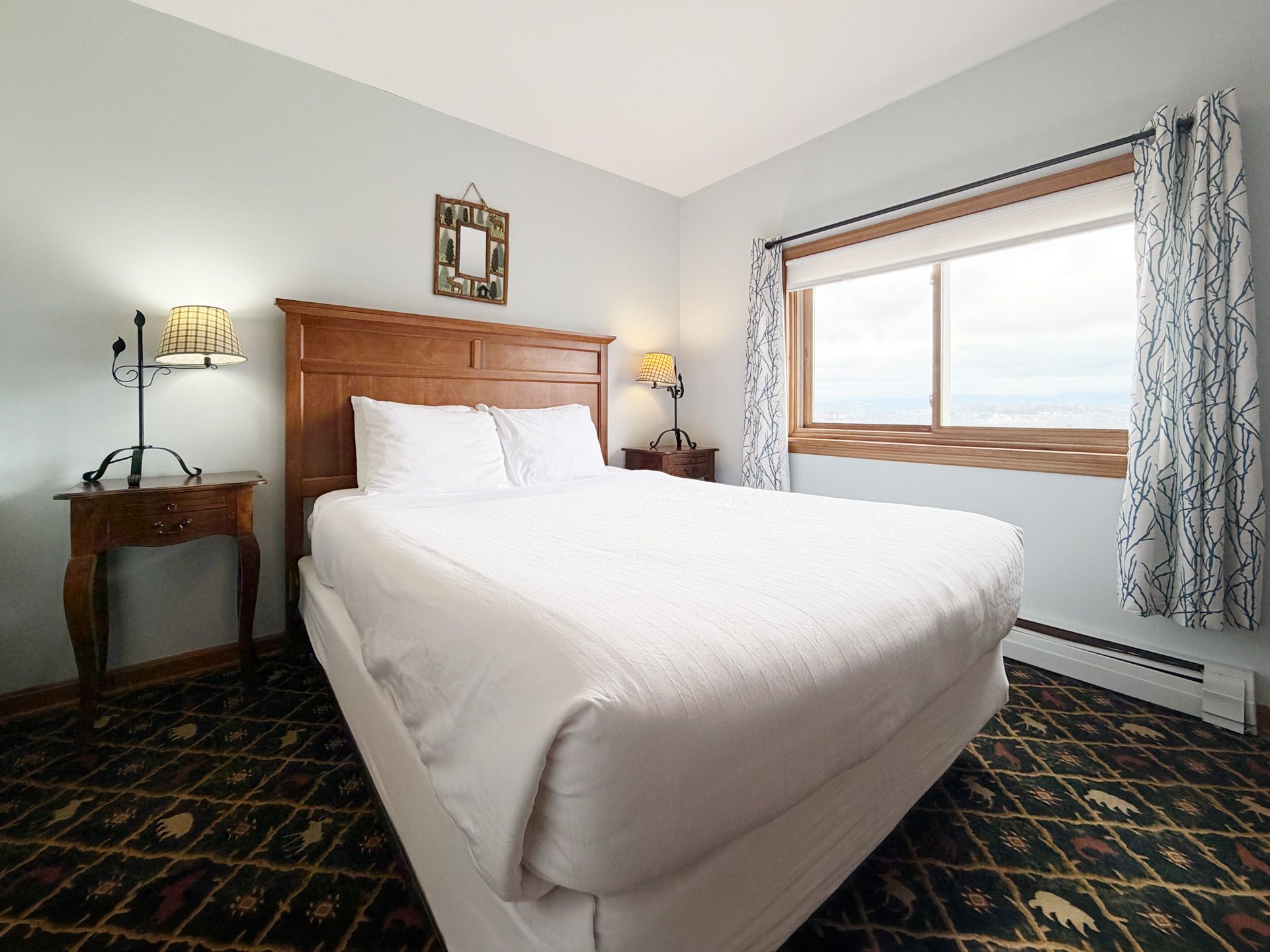 Bright hotel-style bedroom with white bed, wooden headboard, nightstands, and a window with curtains