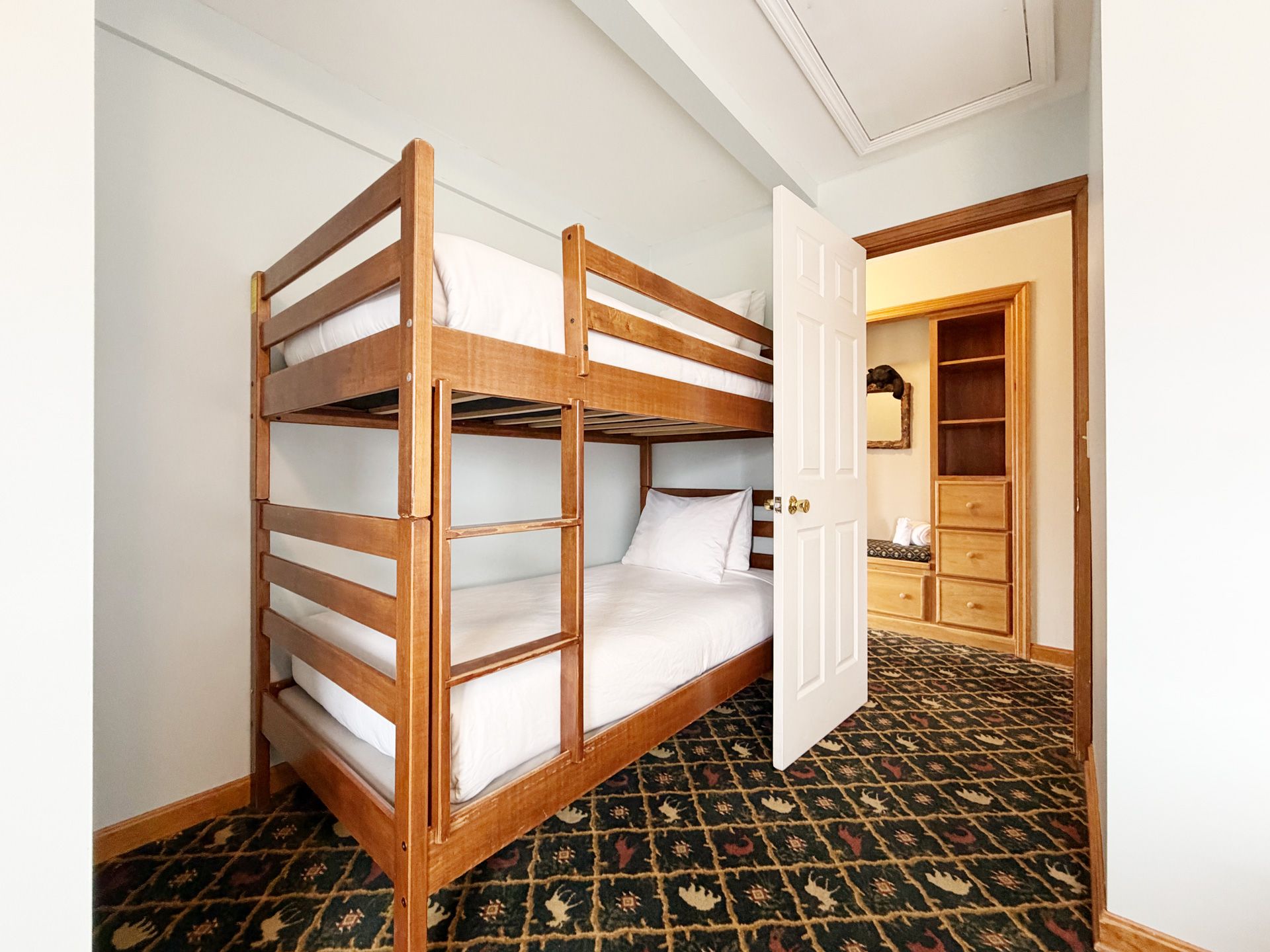 Small bedroom with wooden bunk beds, patterned carpet, and an open door to a closet or dressing area