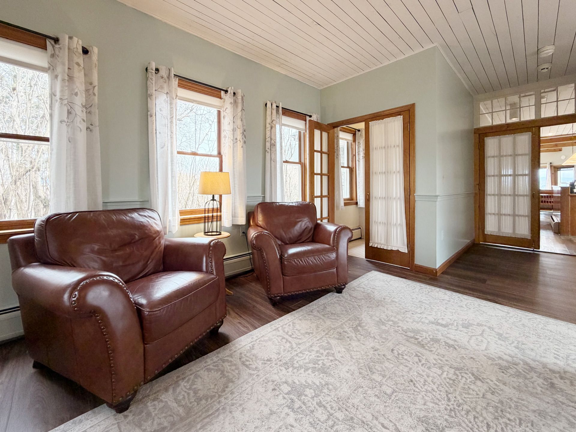 Bright living room with brown leather chairs, white rug, tall windows, and wood trim