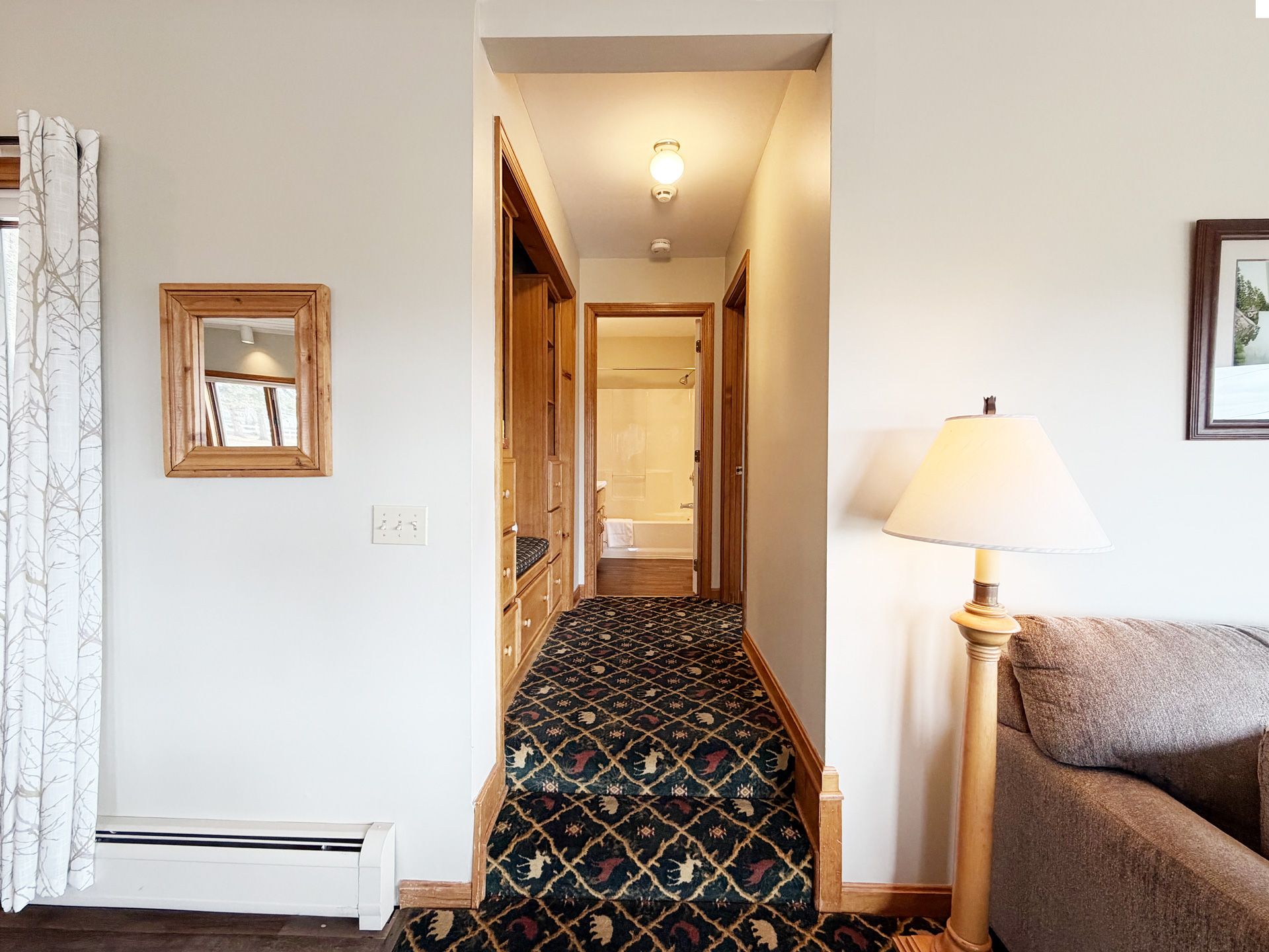 Living room view into a narrow hallway with patterned carpet and a lit lamp beside a sofa