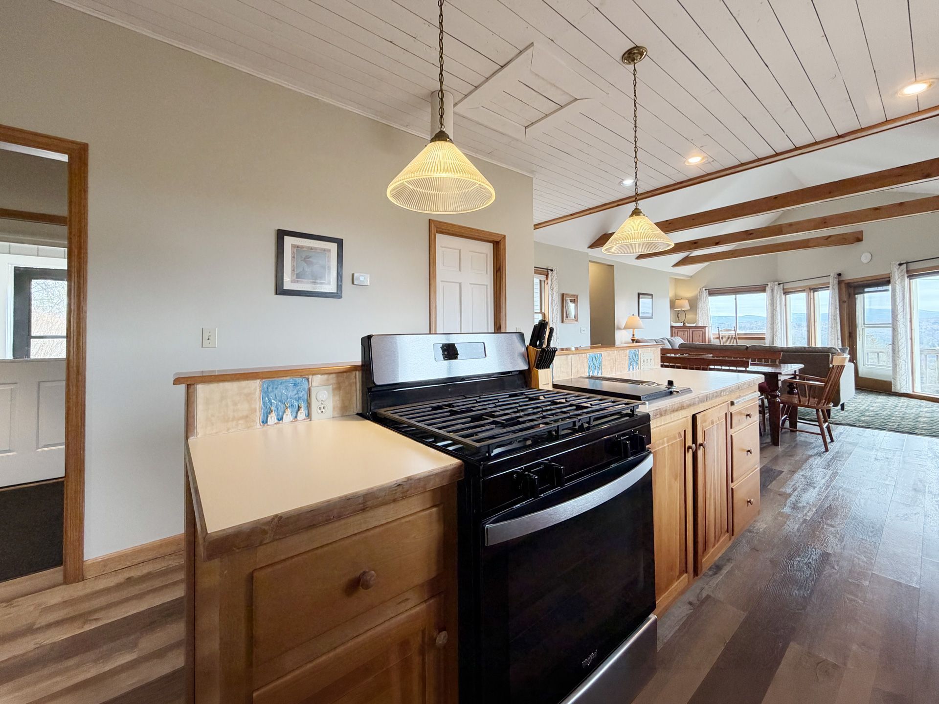 Kitchen with black stove, wood cabinets, pendant lights, and open view to a dining area.