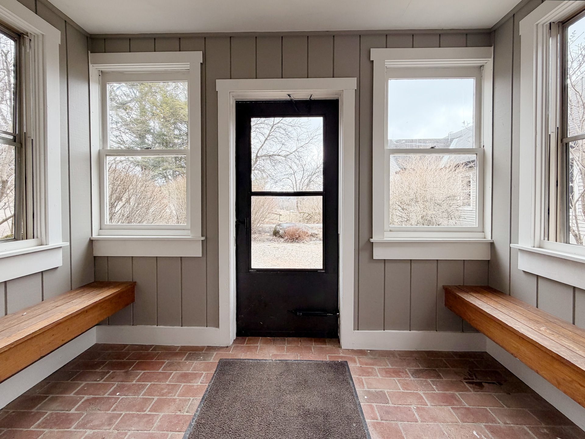 Empty enclosed porch with gray walls, red tile floor, black door, and benches along both sides