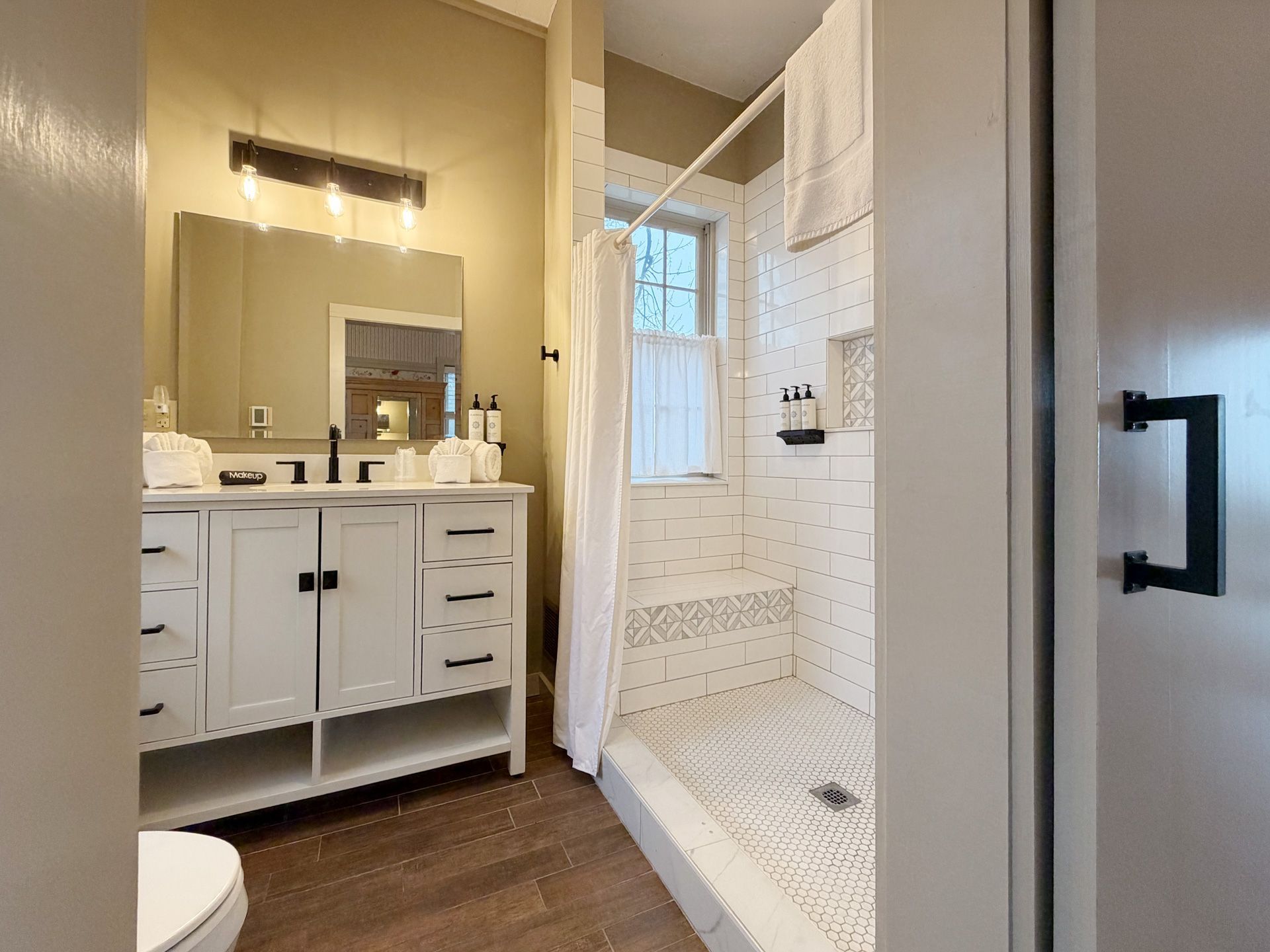 Bathroom with white vanity, mirror lights, and tiled shower with a glass door and window.