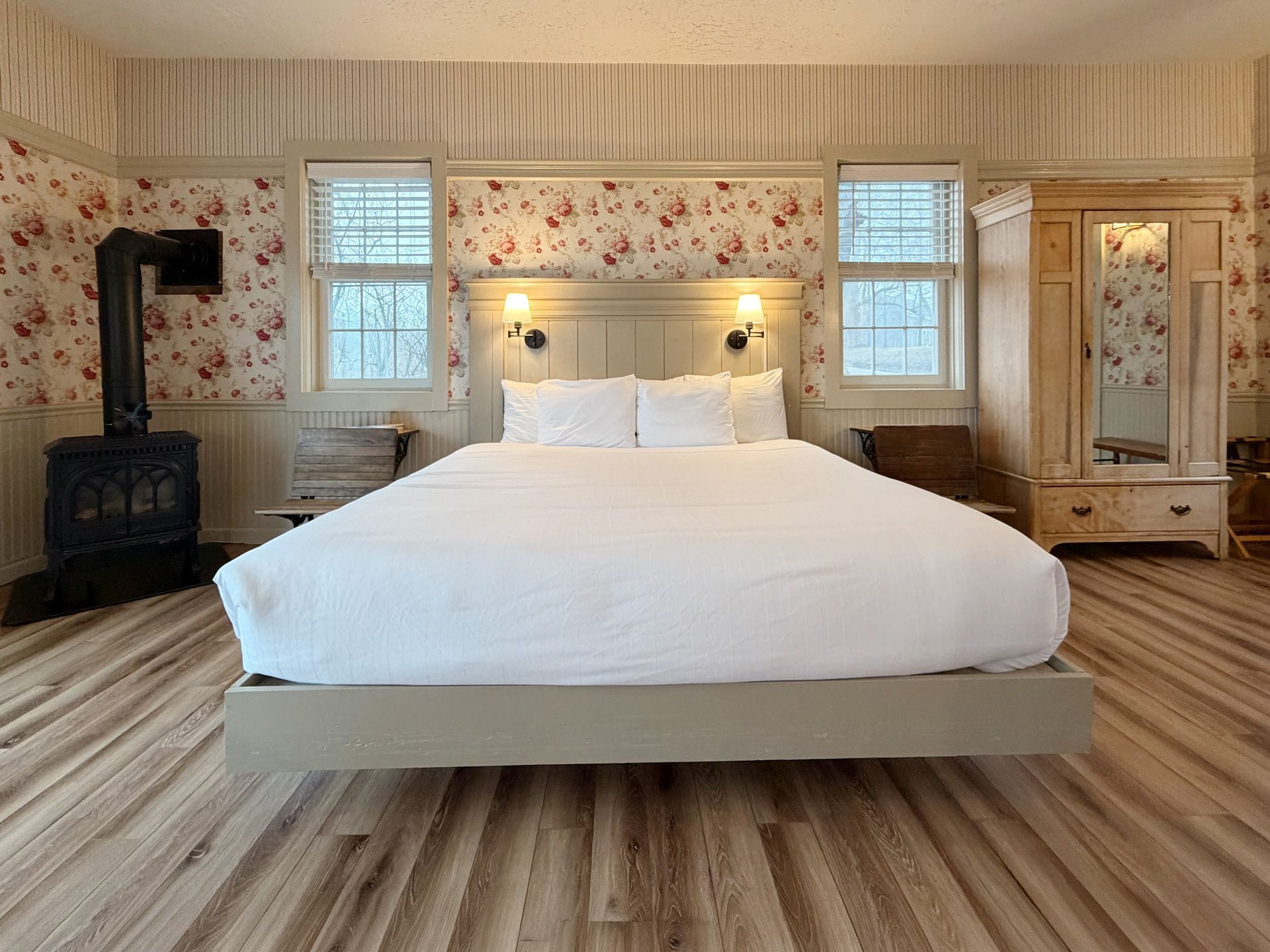 Cozy bedroom with a large bed, floral wallpaper, windows, and a black wood stove