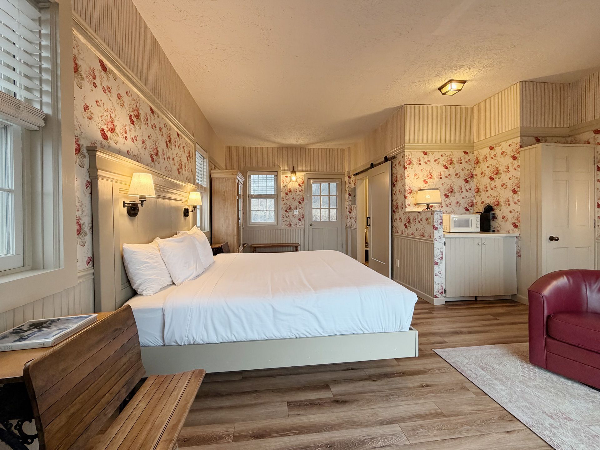 Bright, cozy bedroom with a large bed, floral wallpaper, and a wooden dresser by the window.