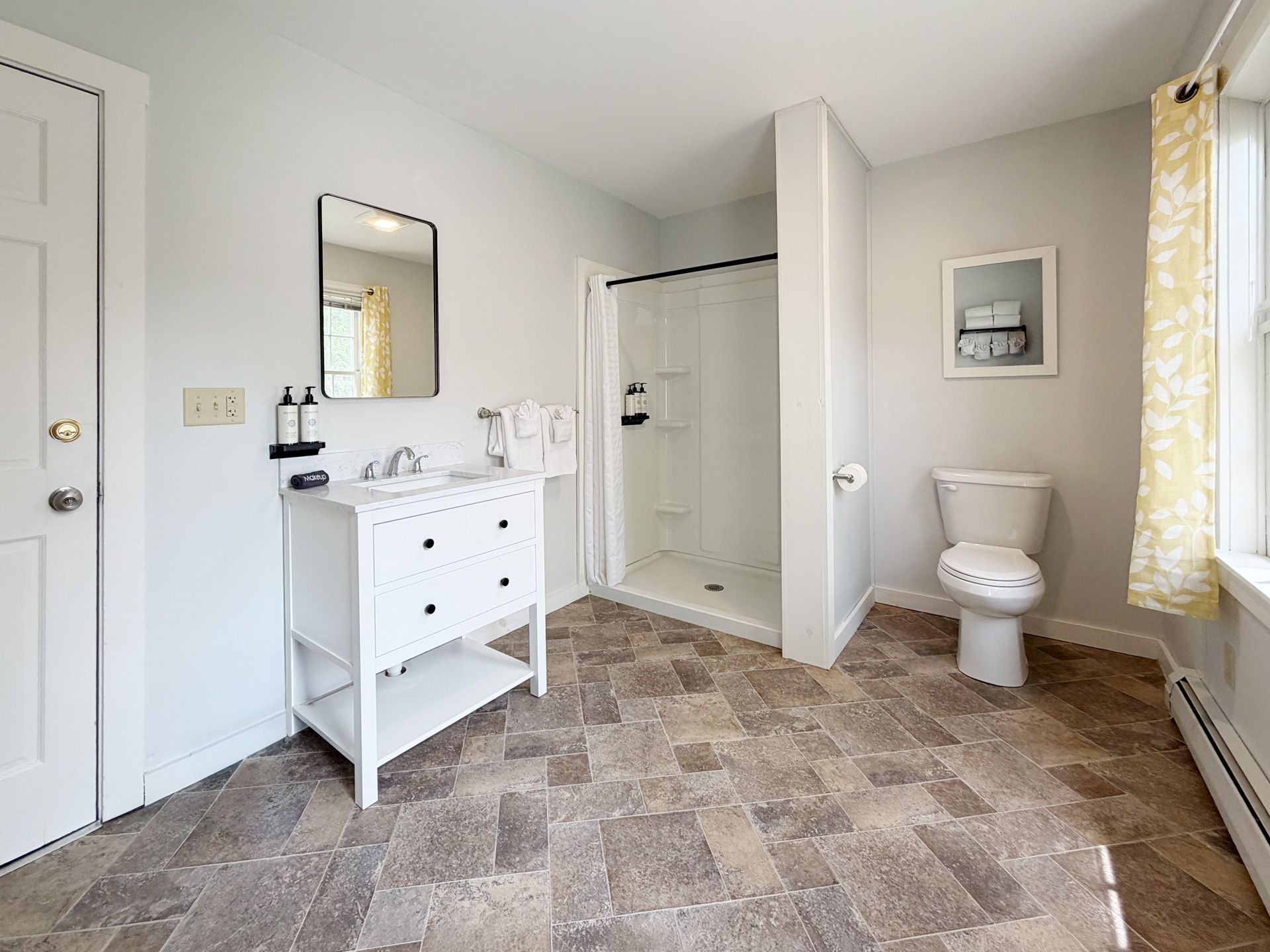Small bathroom with white vanity, toilet, shower stall, and patterned tile floor