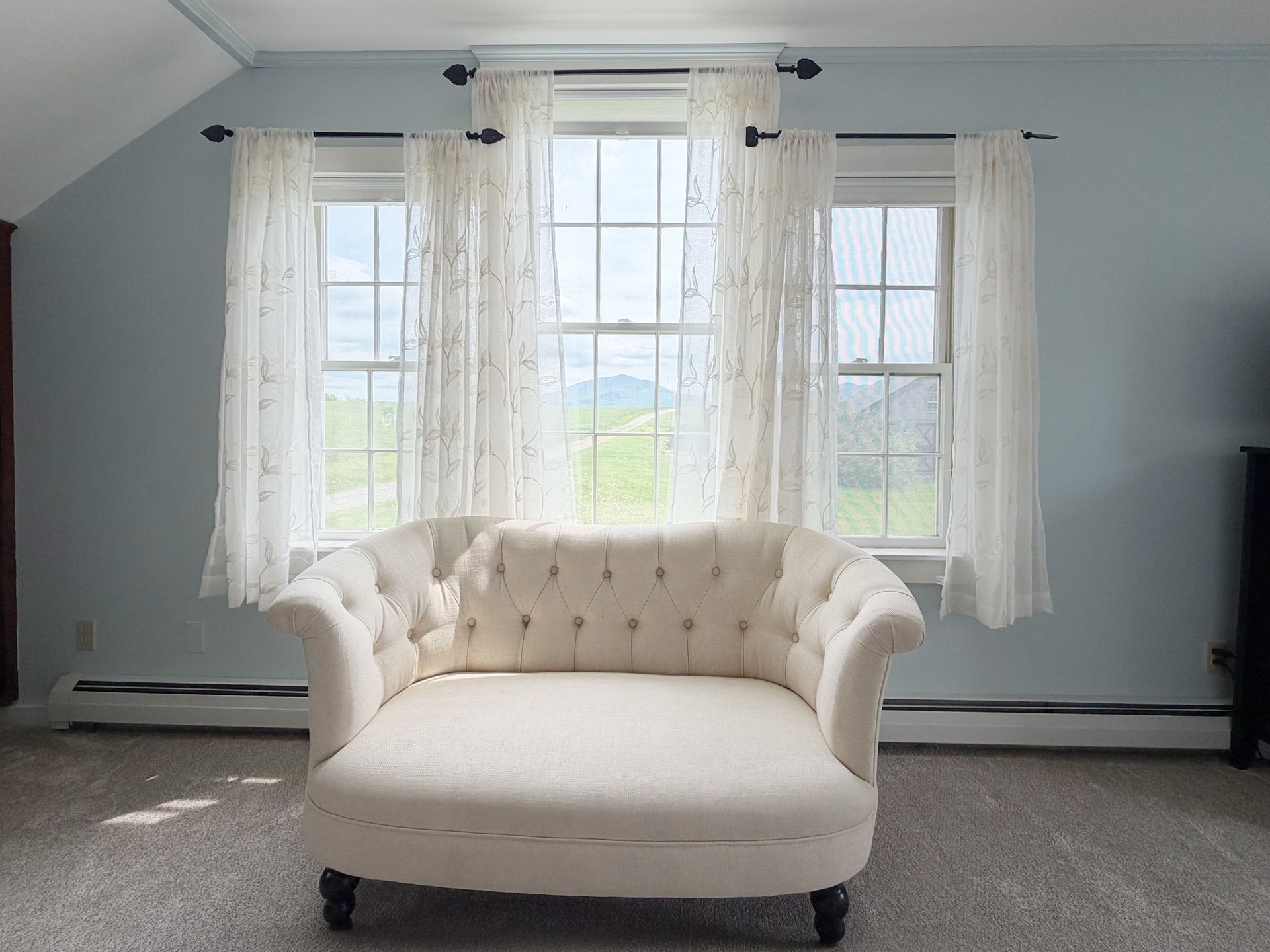 Bright living room with a cream chaise lounge in front of large window and white curtains
