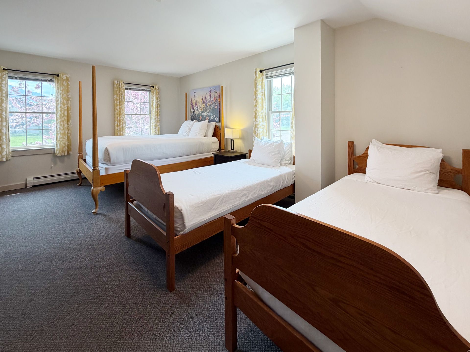 Bright bedroom with three wooden twin beds, white bedding, and large windows on beige walls.