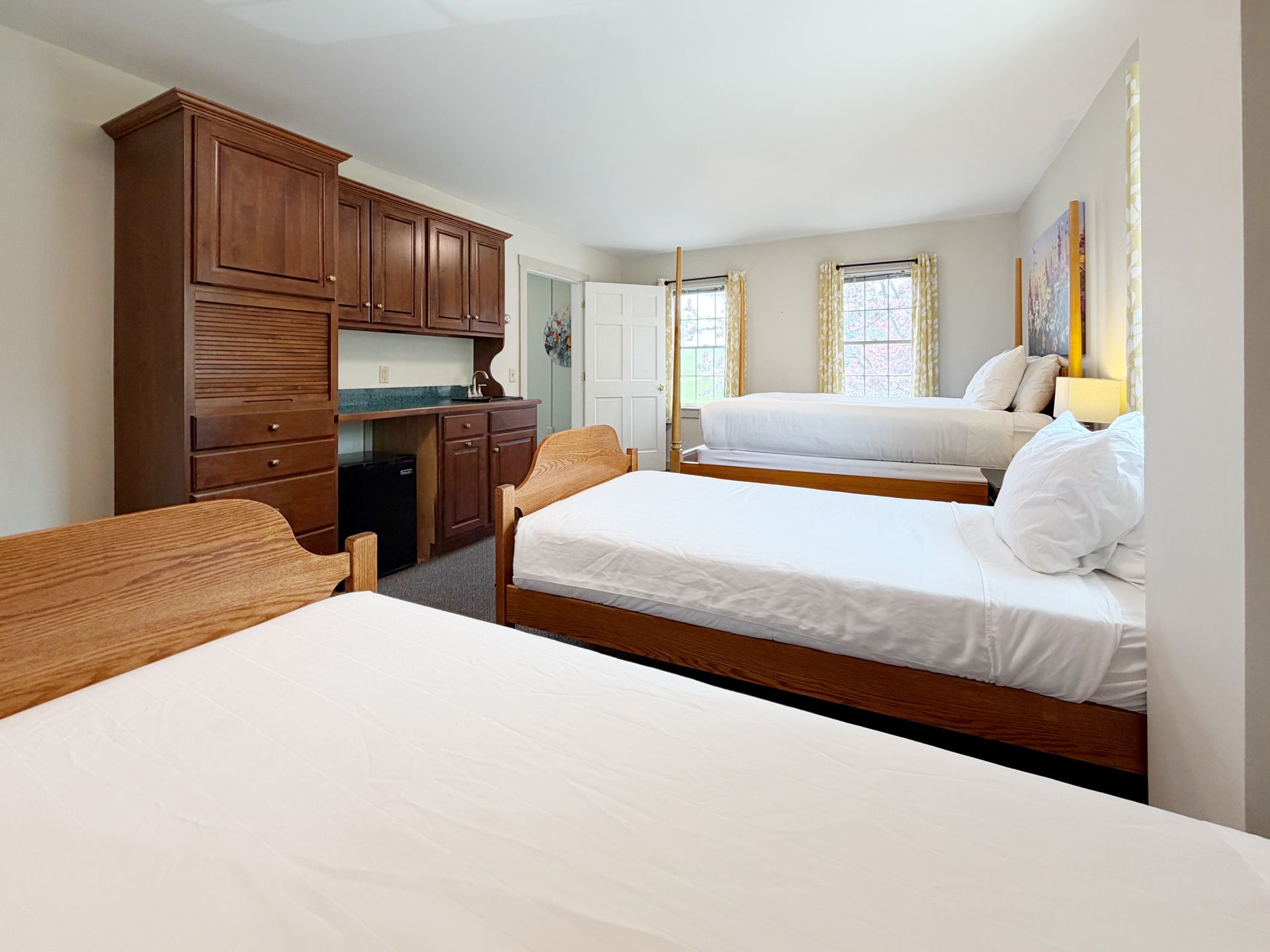Bedroom with four beds, wooden cabinets, and bright windows along the wall