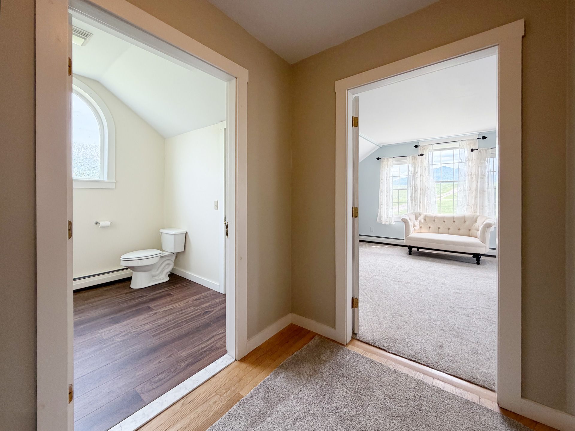 Hallway with open doors to a bathroom on the left and a carpeted bedroom or living room on the right