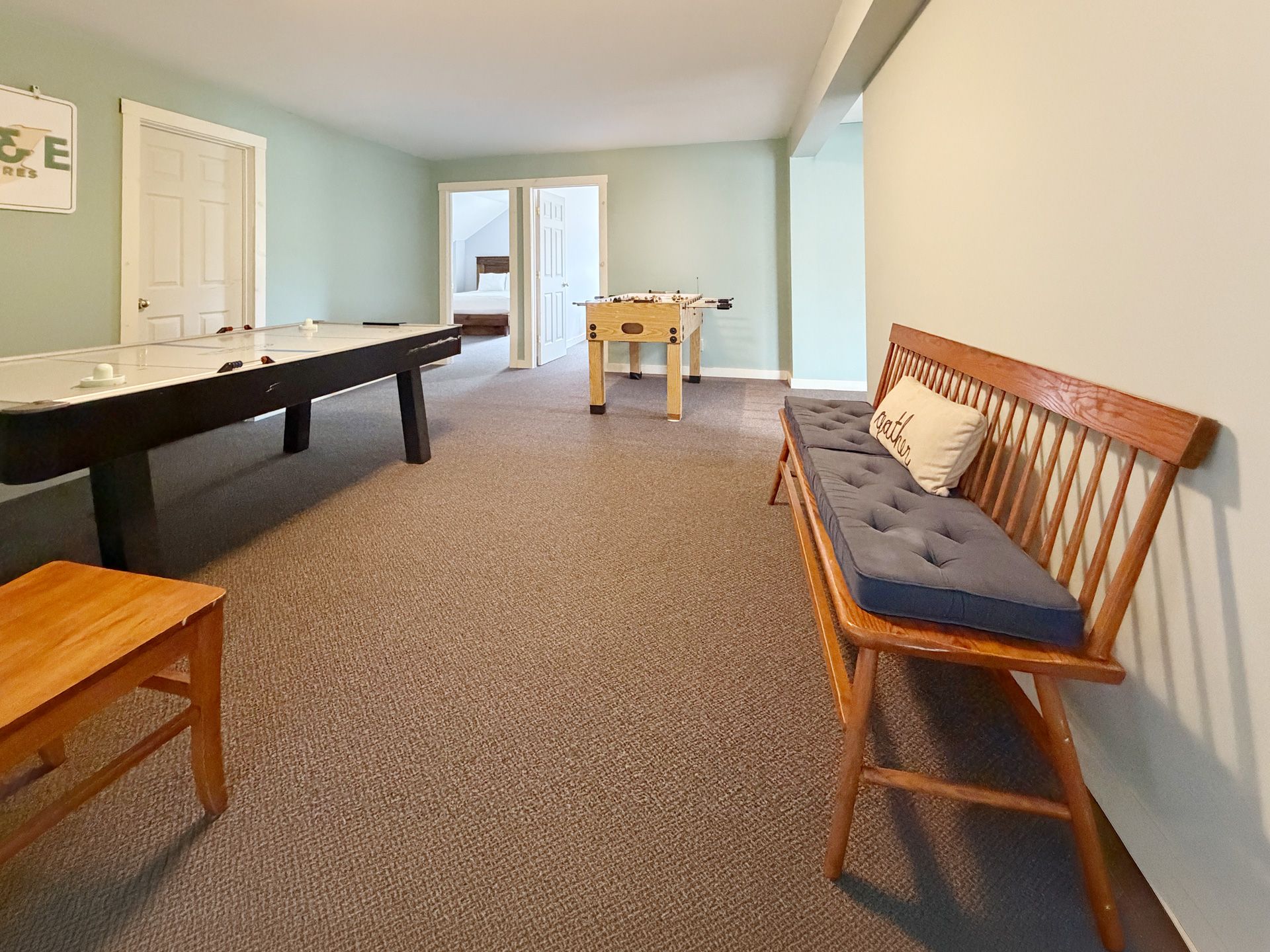 Spacious room with carpet, a pool table, wooden bench, and sunlight through a central doorway.