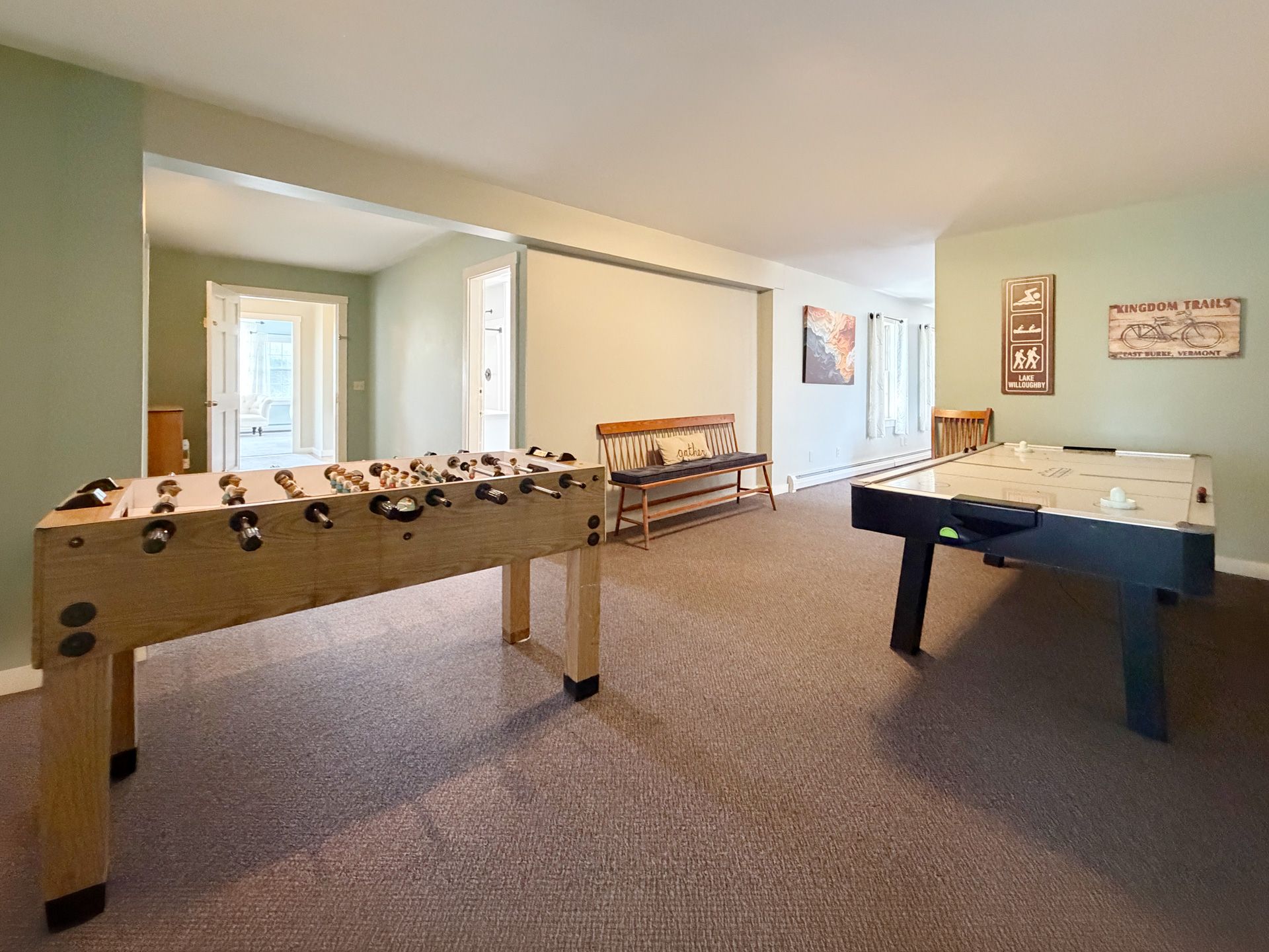 Game room with two foosball tables on carpet in a bright, green-walled basement.