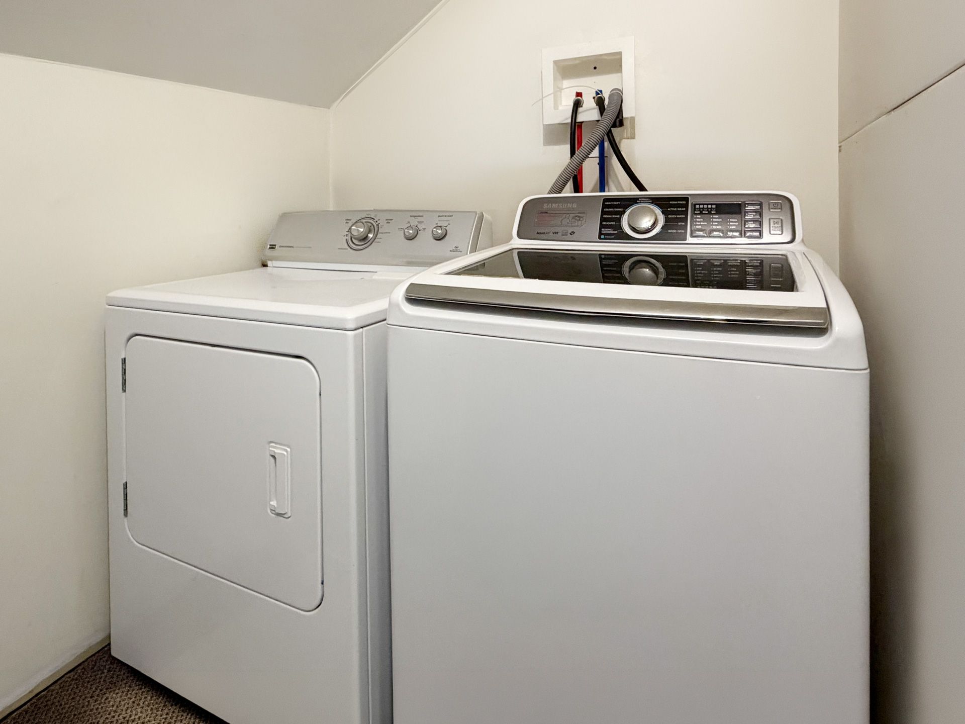 White washer and dryer in a small laundry room under sloped walls