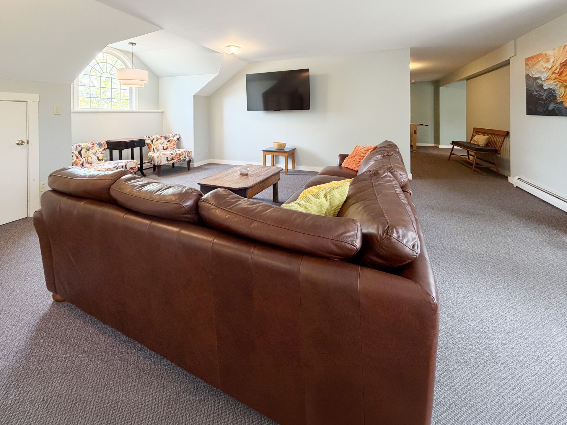 Spacious living room with brown sectional sofa, wall-mounted TV, gray carpet, and arched window seating.