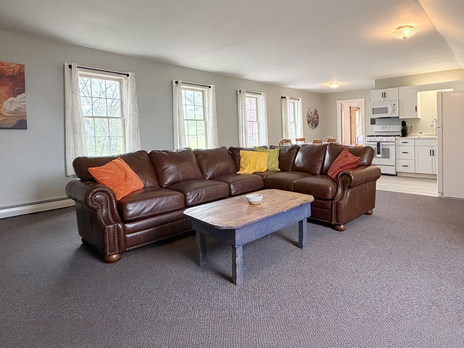 Living room with brown leather sectional, coffee table, and carpeted floor near kitchen.