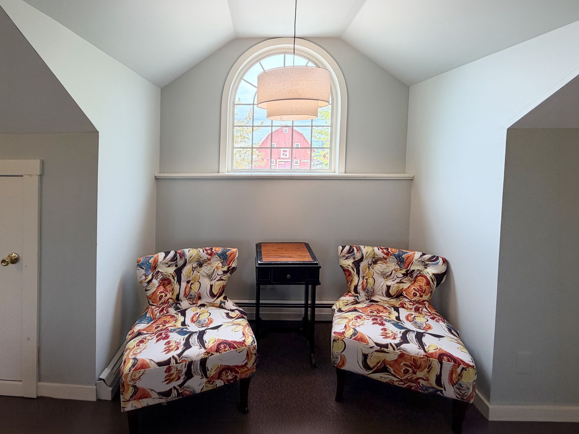 Two floral chairs beside a small table under an arched window in a bright alcove.