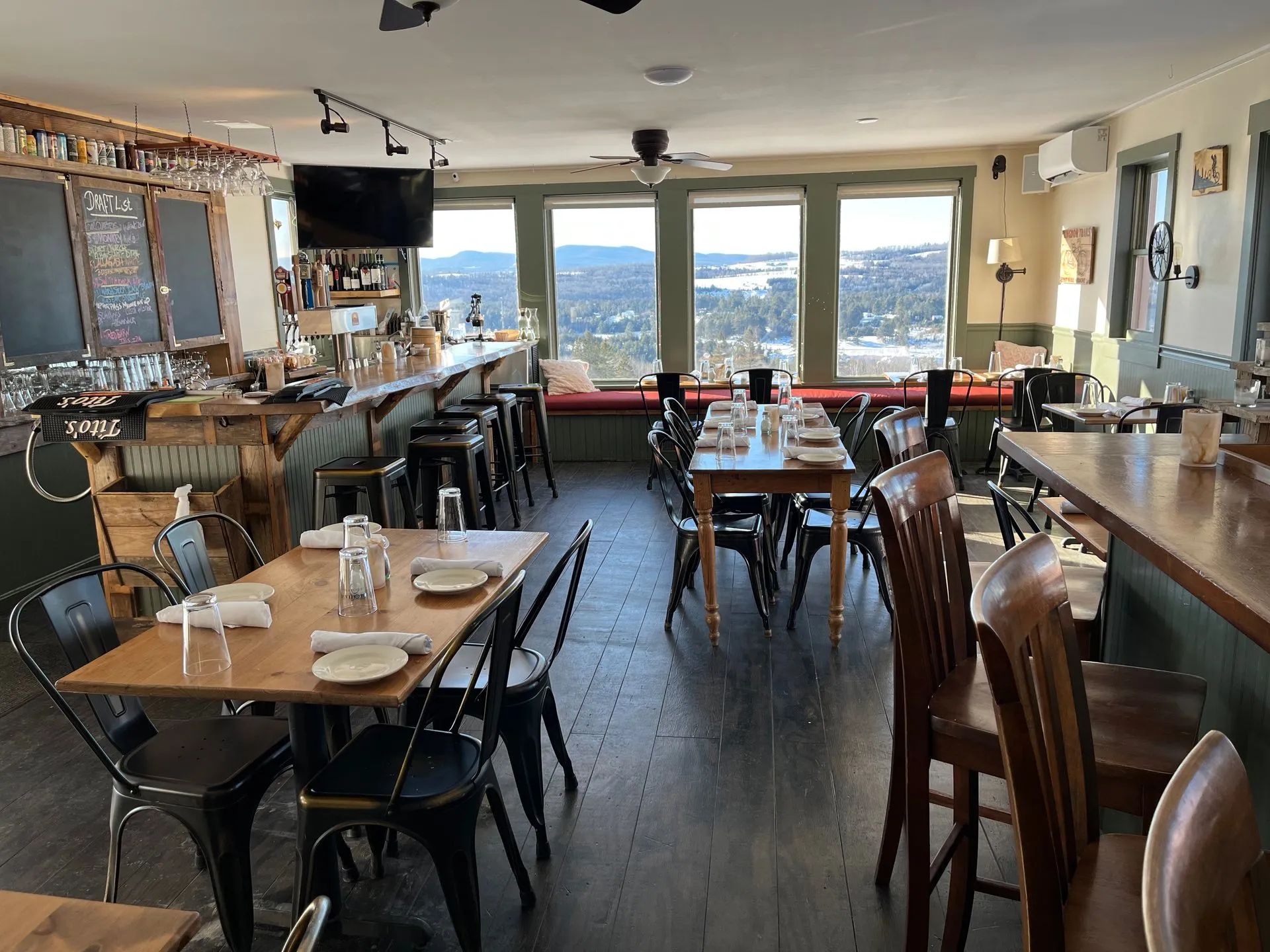Restaurant dining room with wooden tables, chairs, and large windows overlooking a city skyline