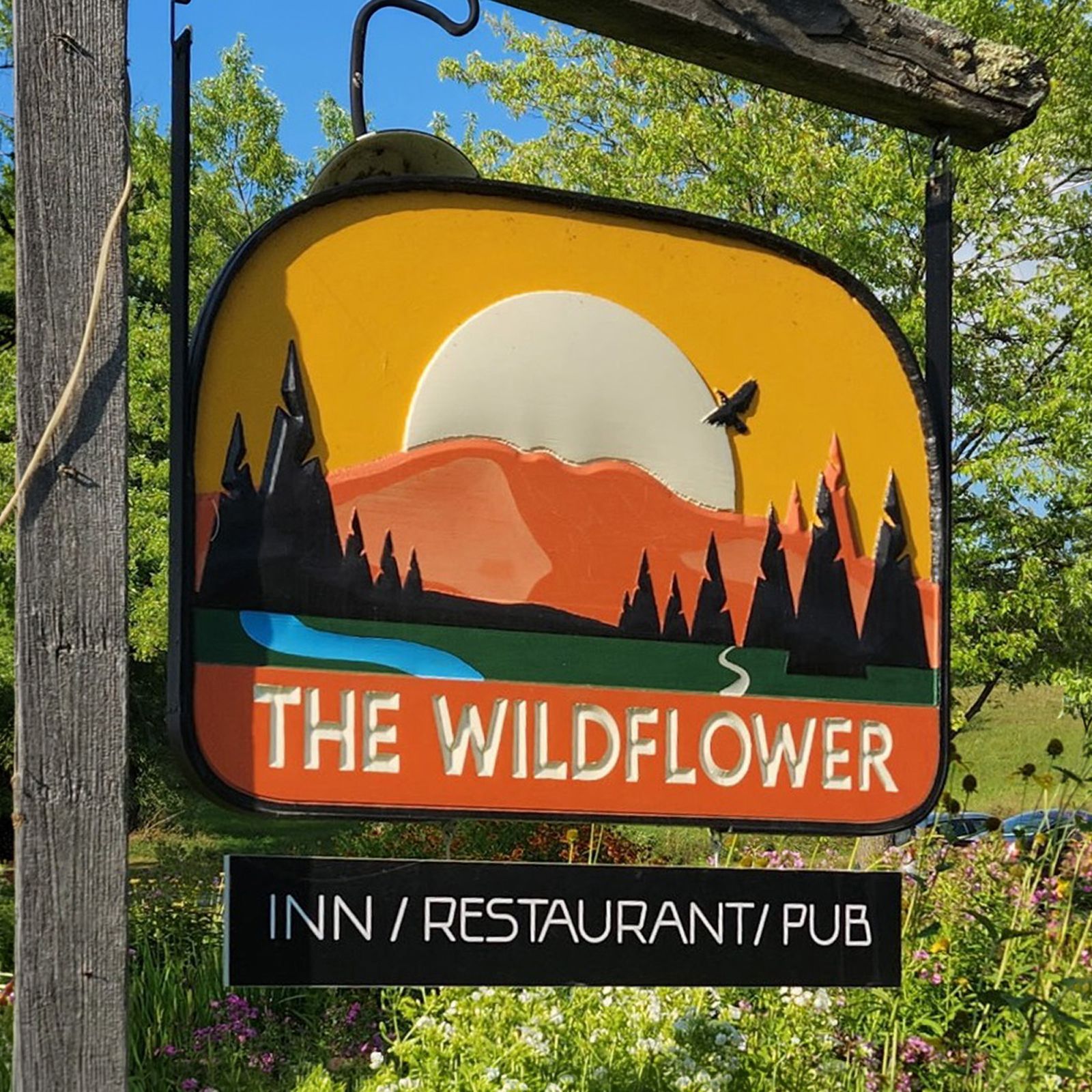 Sign for The Wildflower inn, restaurant, and pub with orange sunset and mountains