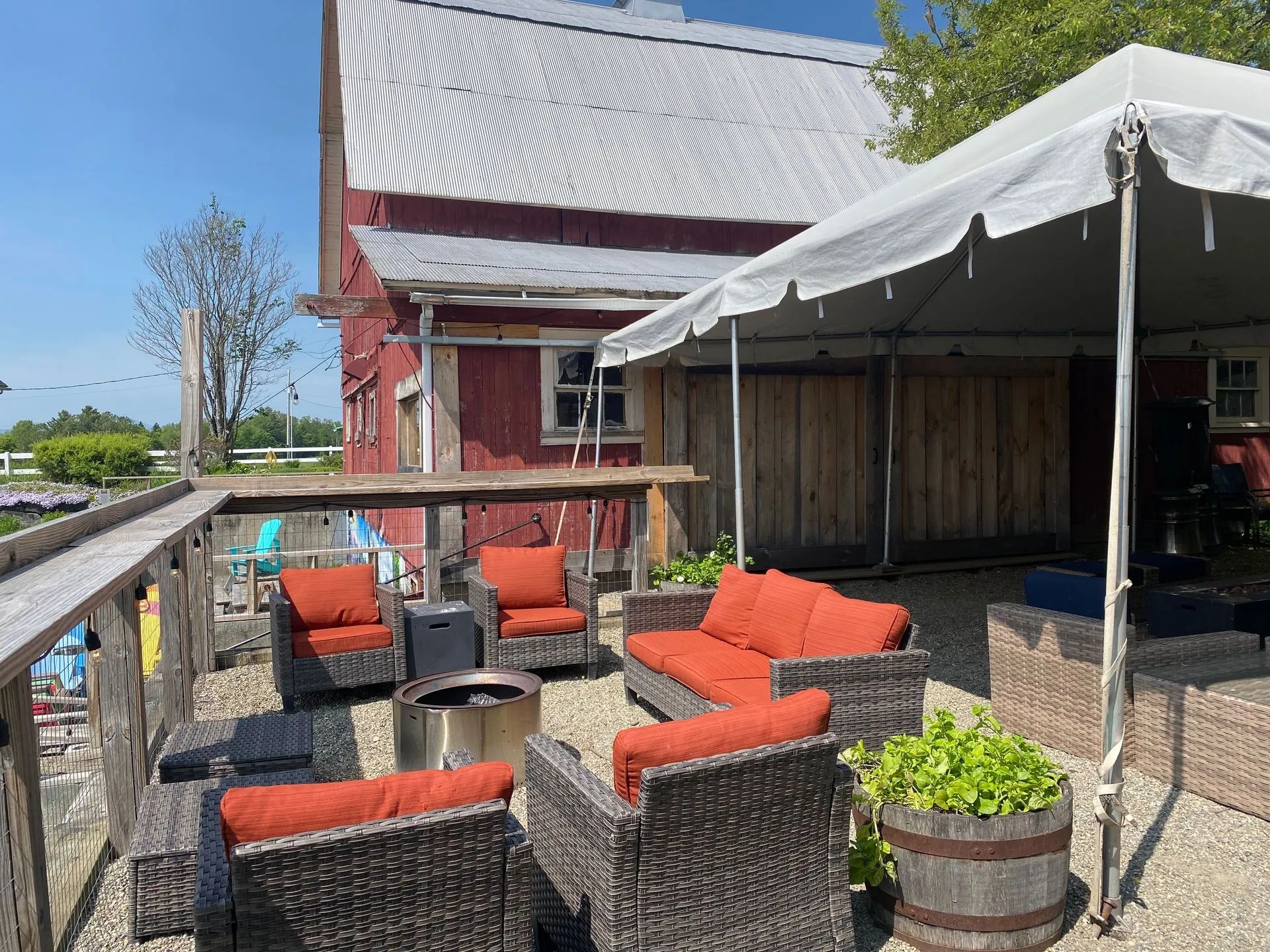 Outdoor patio with red cushioned wicker chairs, tables, and a white canopy beside a red building.