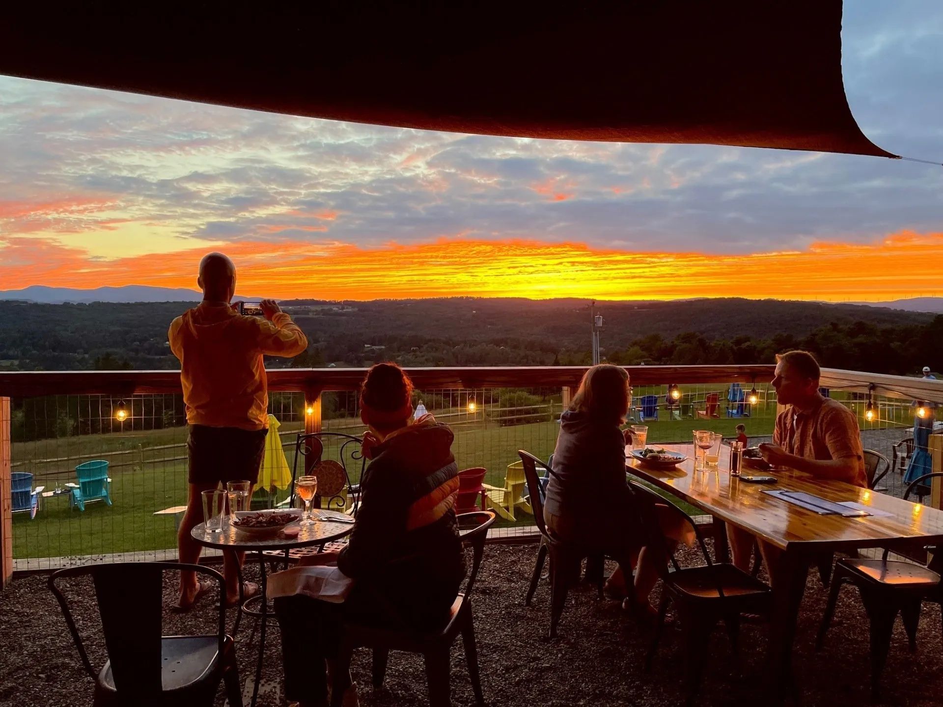 Guests enjoying dinner at sunset on the back deck of The Wildflower Inn in Lyndonville, Vermont, ove