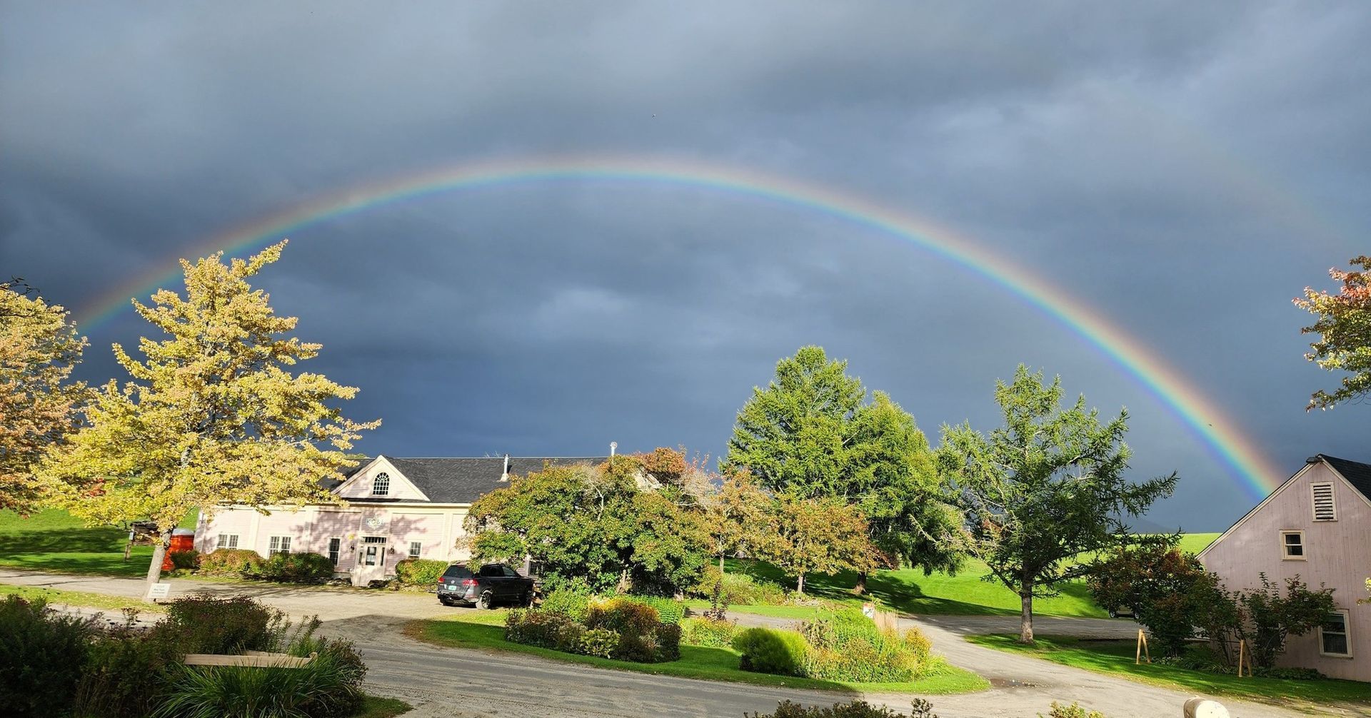 Rainbow over a suburban neighborhood with houses, trees, and a sunlit road after rain
